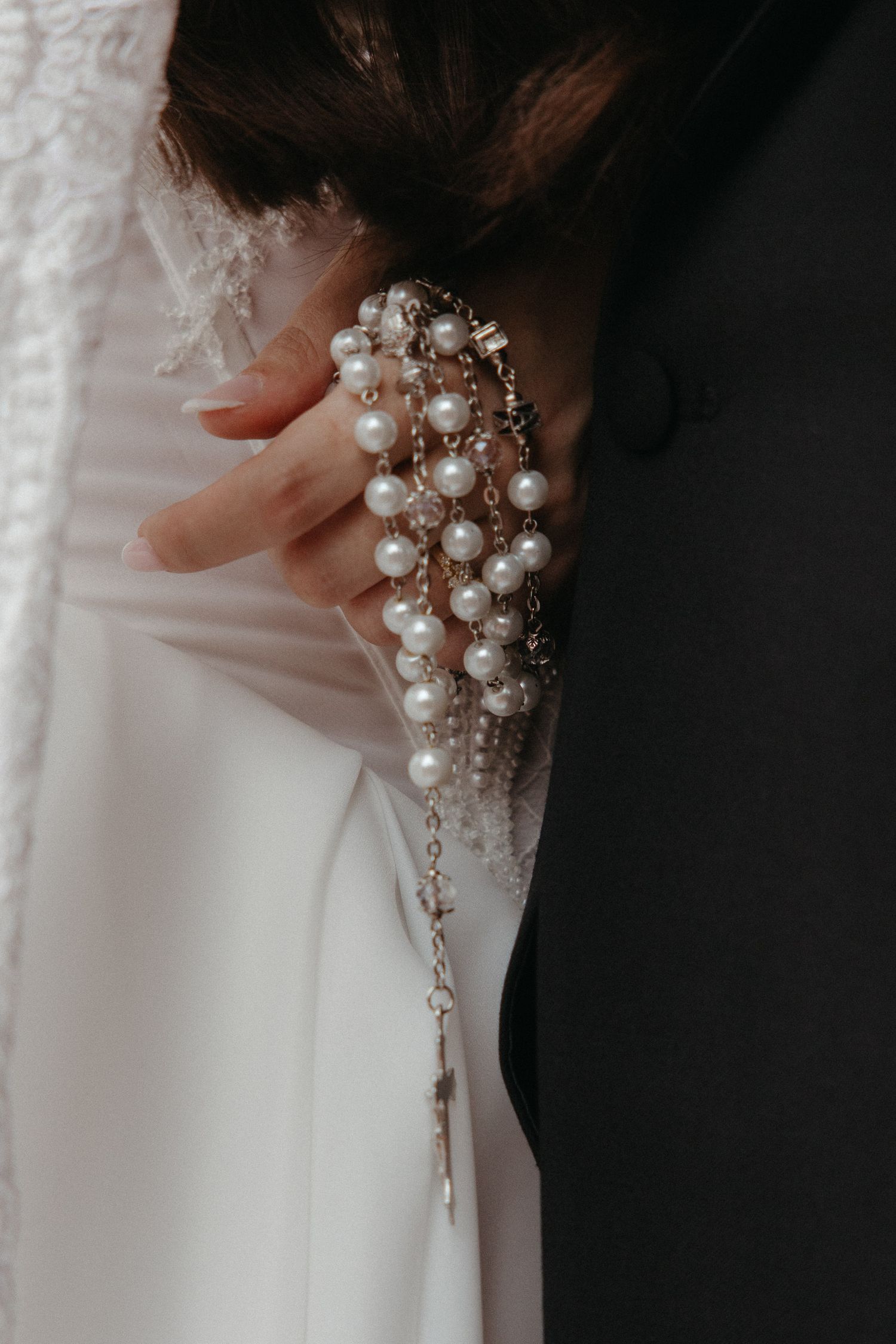 Bride holding pearl bracelet jewelry against white wedding dress, elegant bridal accessory detail photo.