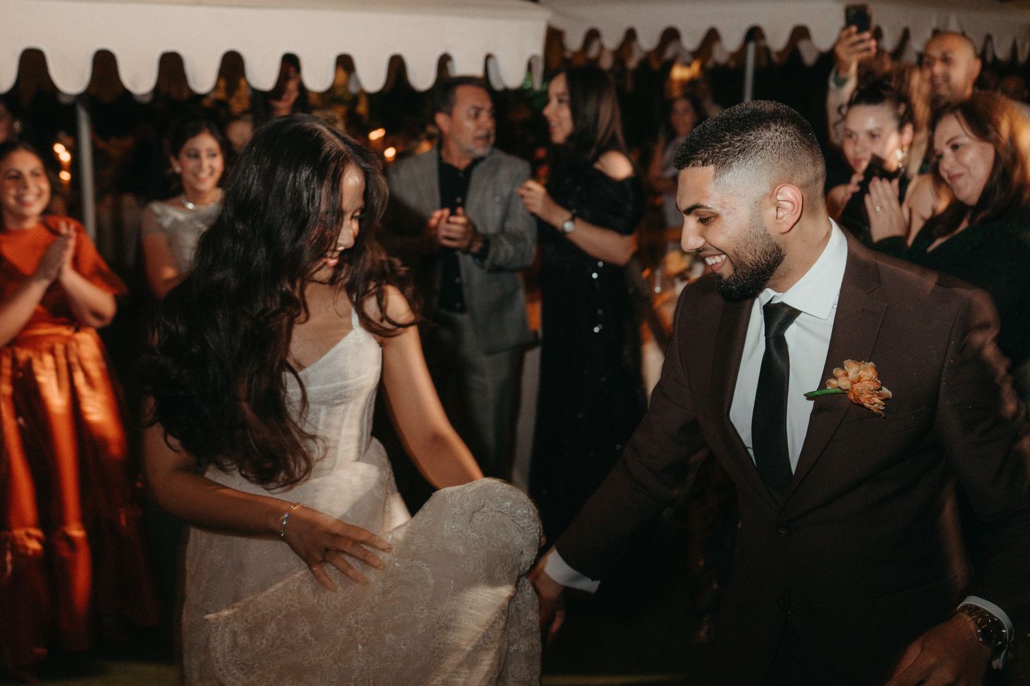 Bride and groom share a joyful first dance at their wedding reception surrounded by celebrating guests.