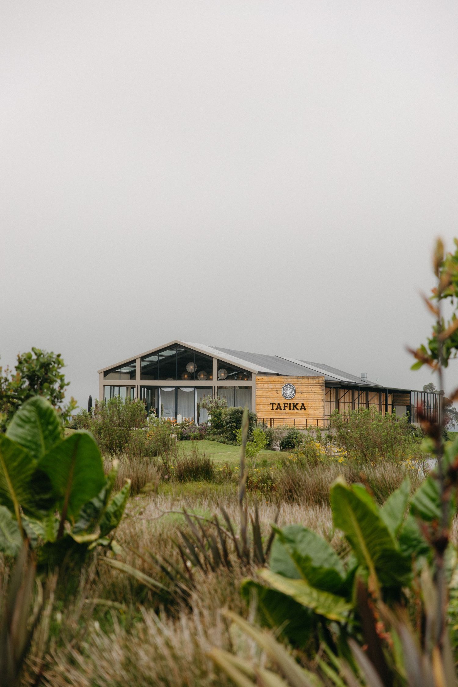 Tafika Polo Farm building surrounded by lush greenery and wetland grasses under an overcast sky.