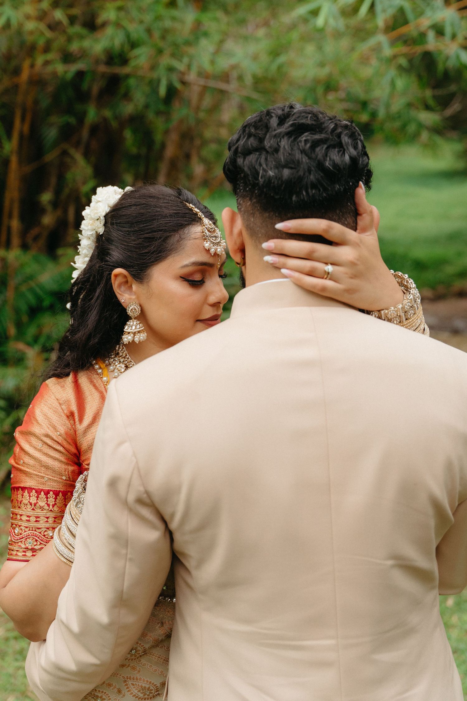 A couple in traditional Indian wedding attire share an intimate moment in a garden setting.