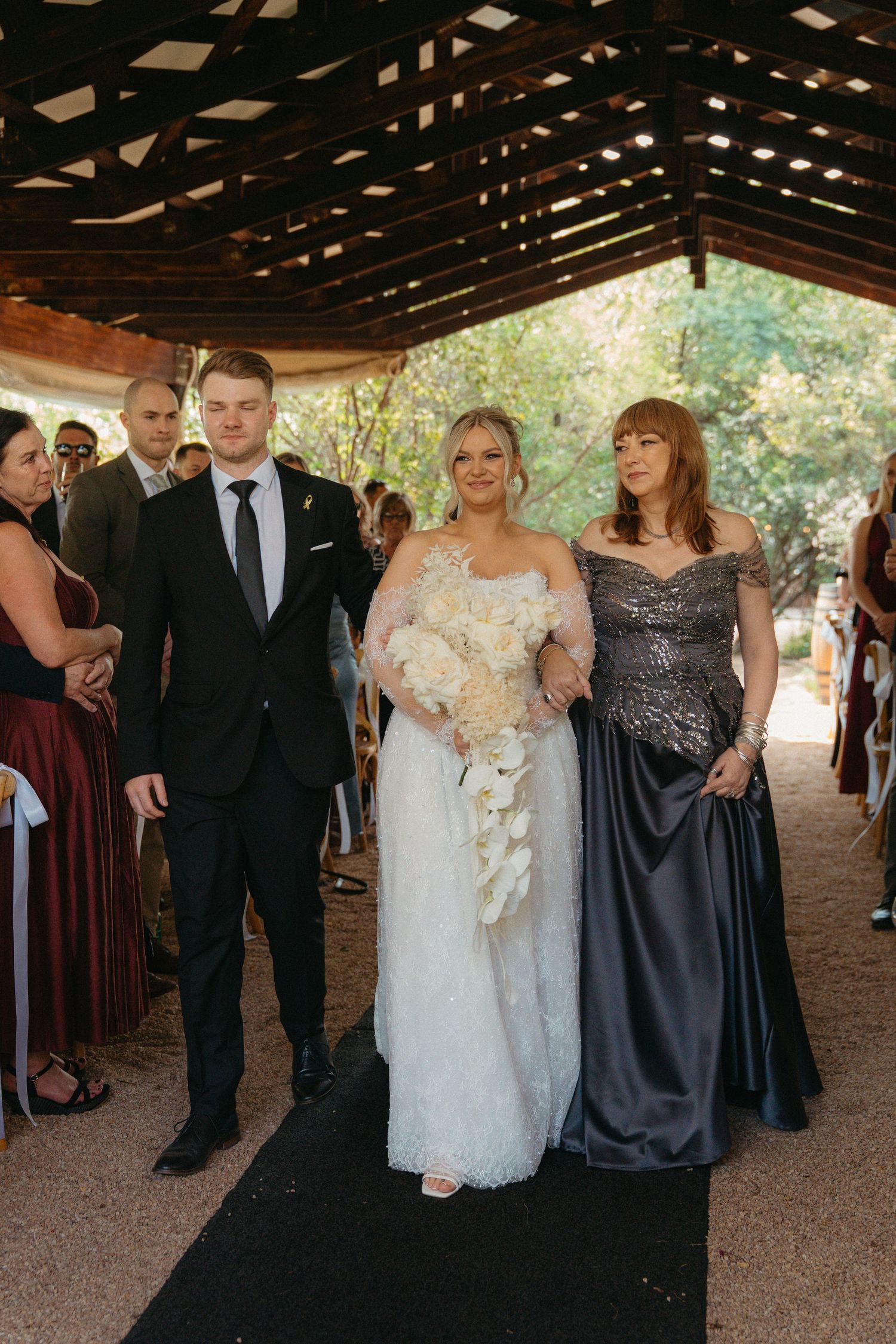 Wedding party walking together under a rustic wooden pavilion with warm lighting and natural outdoor surroundings.