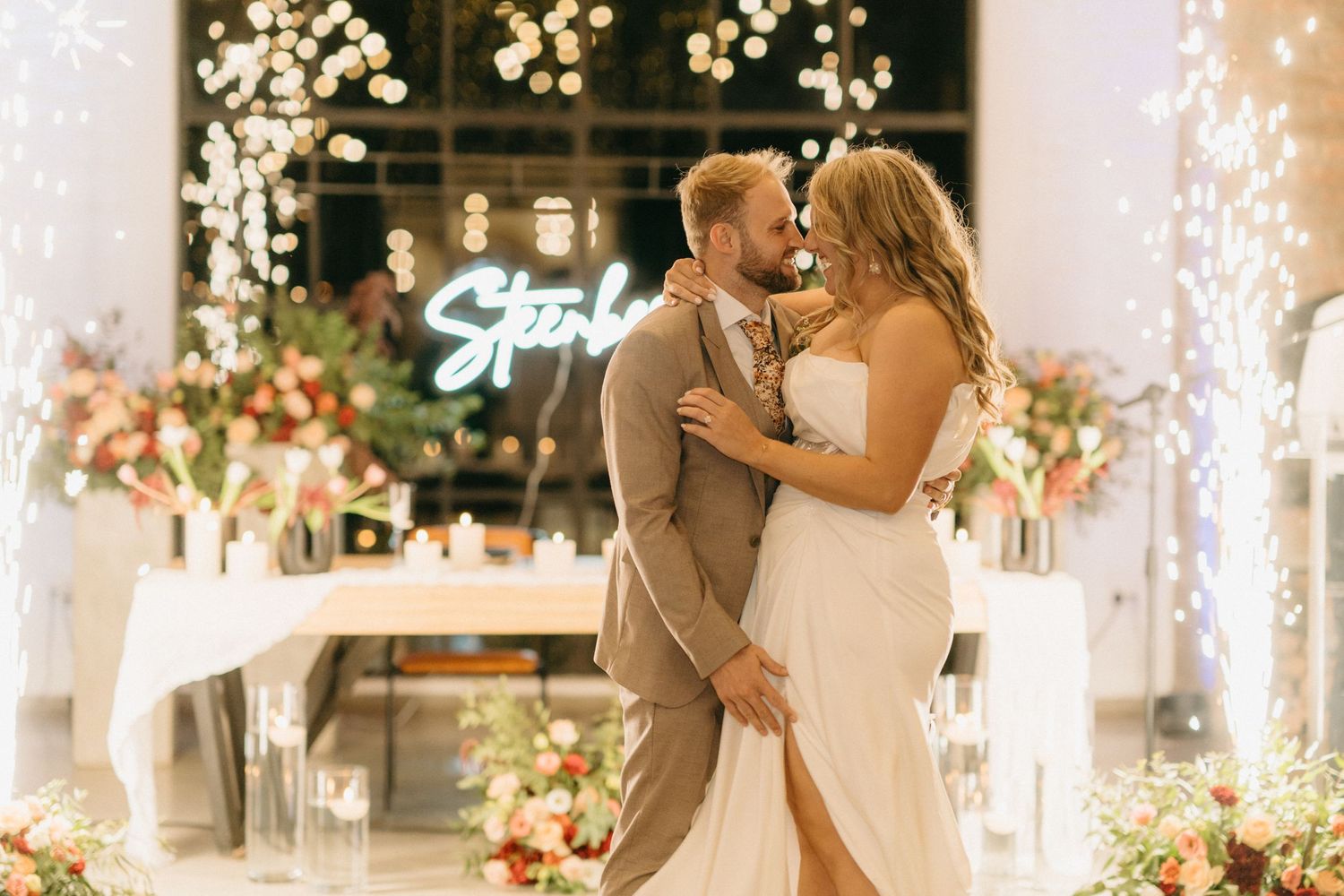 A romantic wedding scene with a neon sign and sparkling pyrotechnics creating a magical atmosphere during a special moment.
