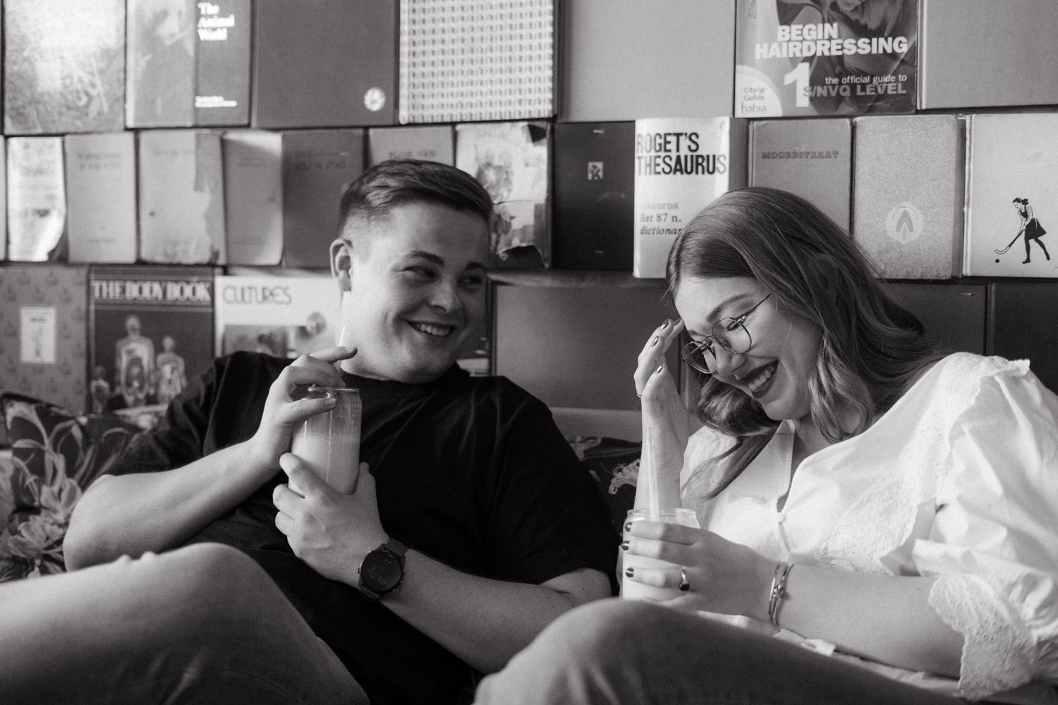 Two people laugh together while enjoying milkshakes in black and white photo.