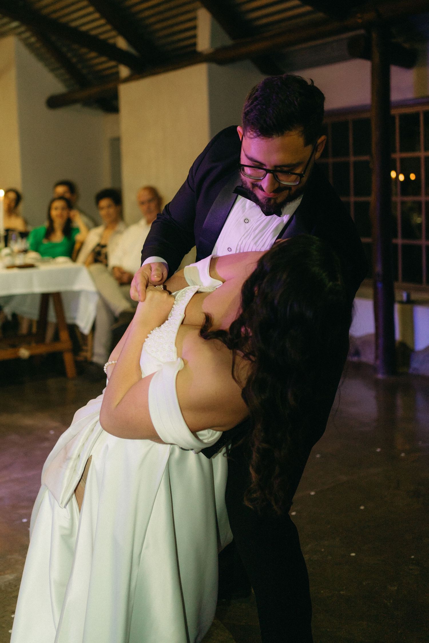 A couple shares an intimate dance dip at their wedding reception while guests look on in the background.