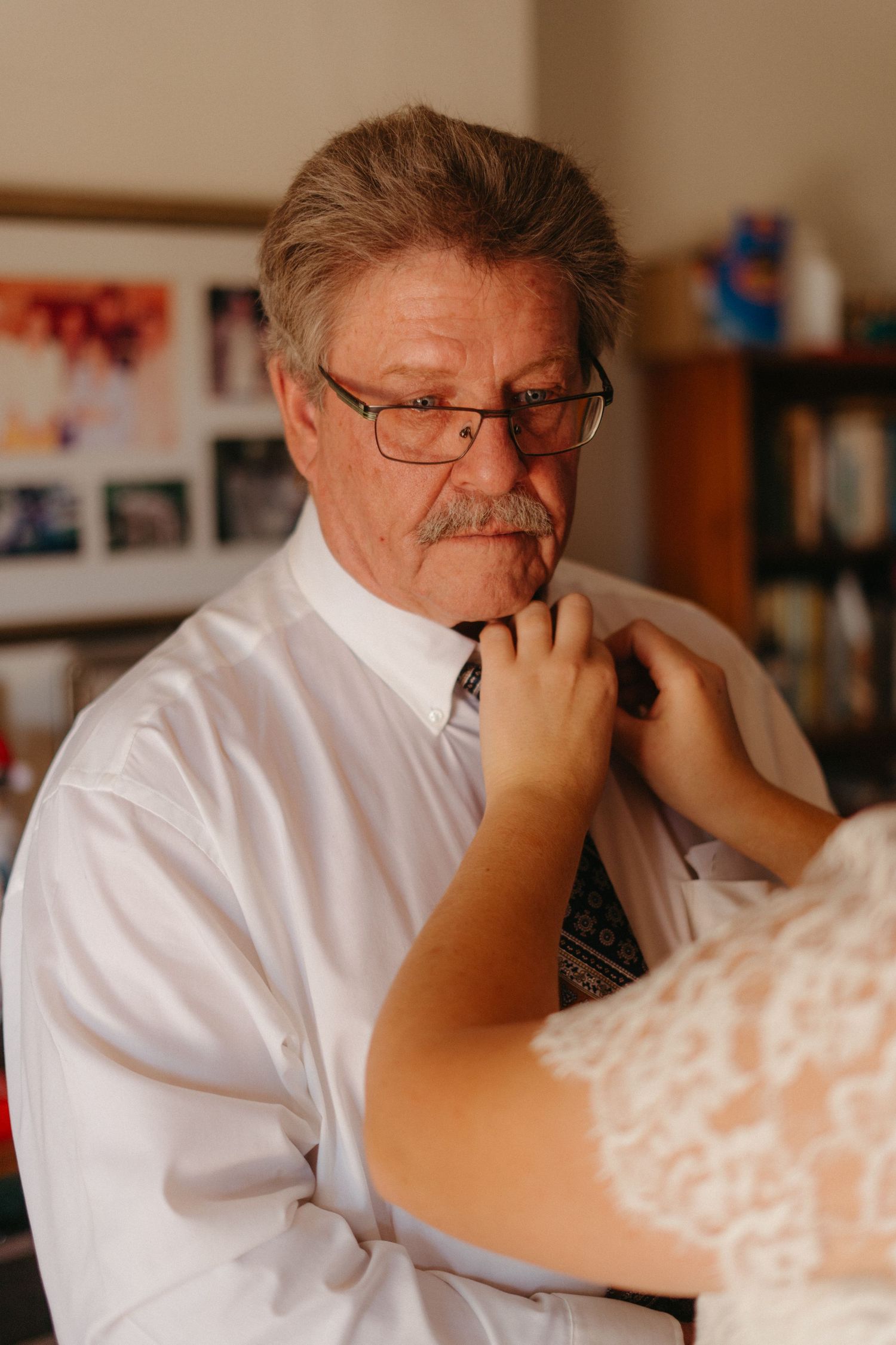 Someone having their tie adjusted while wearing glasses and a white dress shirt.