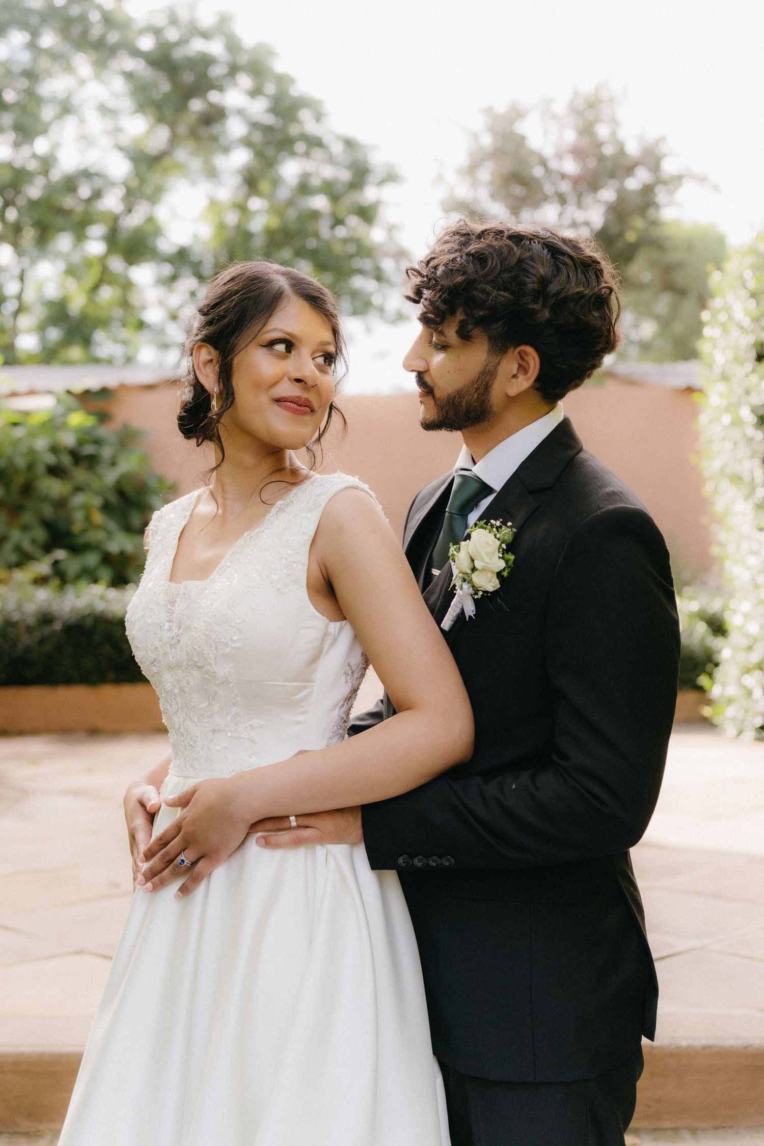 Bride and groom share a romantic embrace against a garden backdrop on their wedding day.
