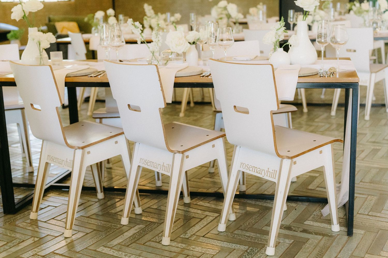 Modern white dining chairs with wooden accents arranged at wedding reception tables in an elegant venue.