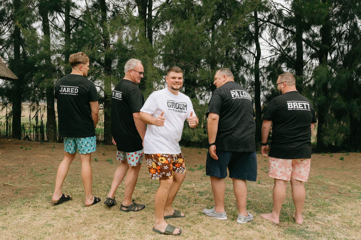 Wedding party members lined up showing their colorful shorts against a natural backdrop.