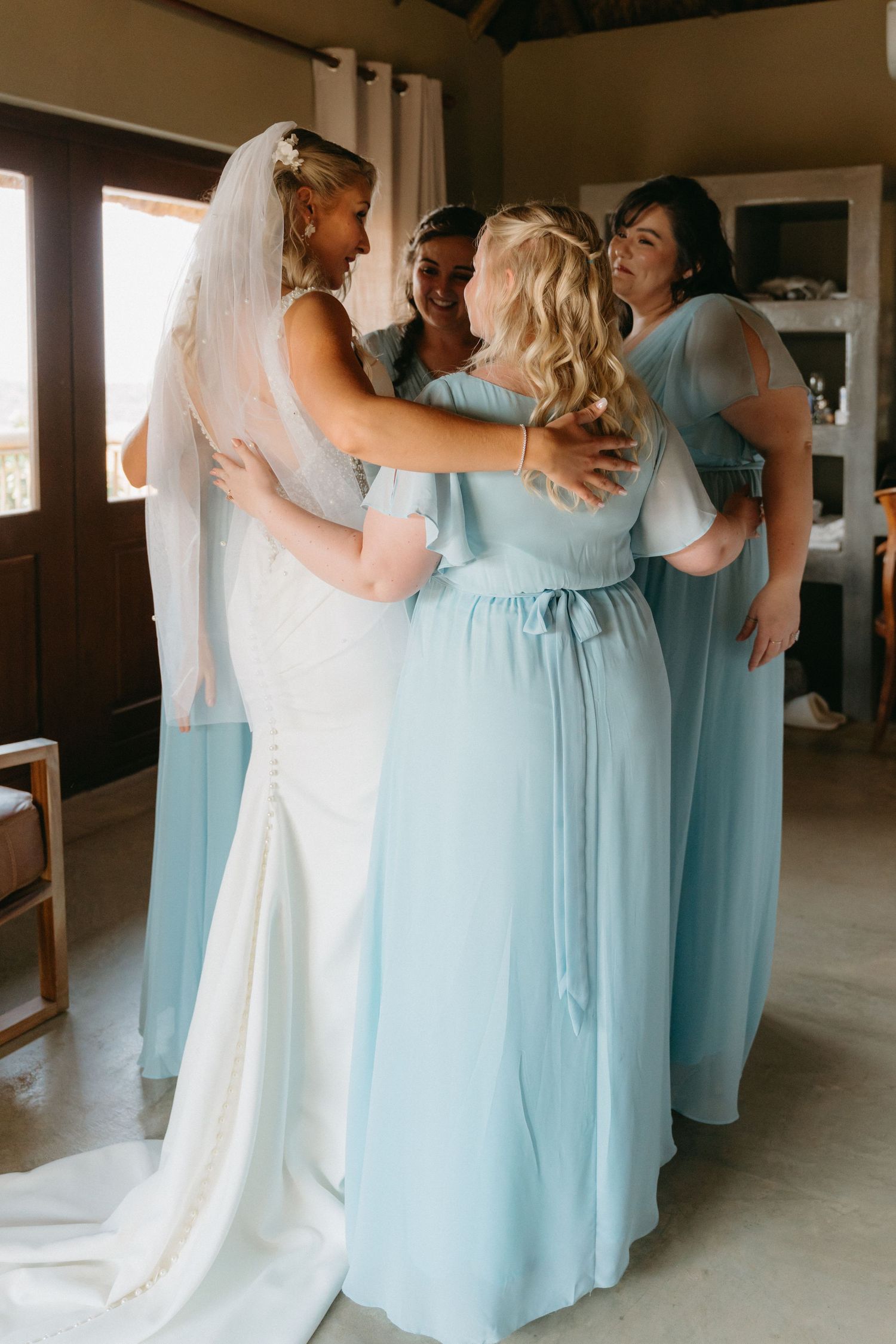 Bridesmaids in light blue dresses embrace in an indoor venue.