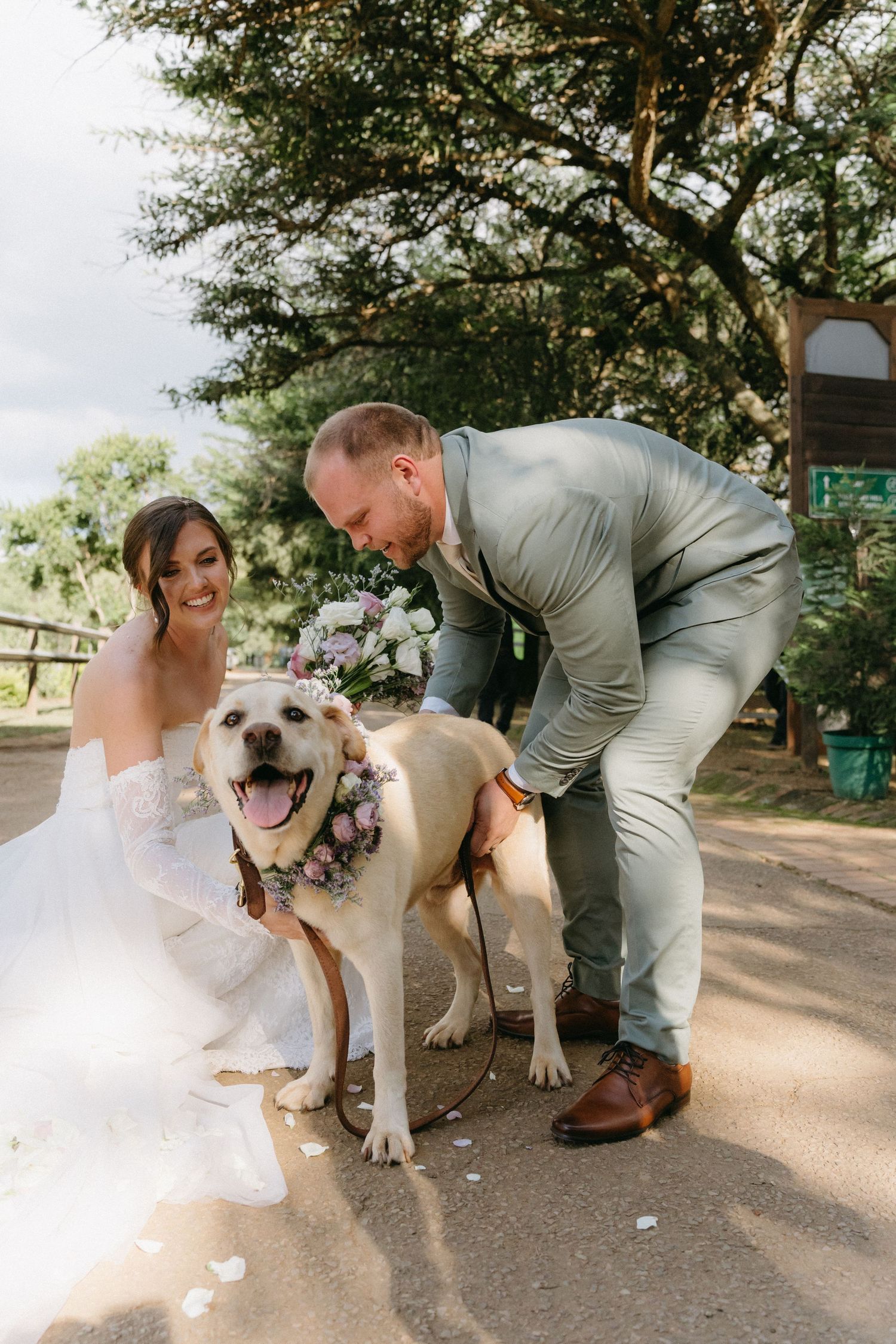 Happy couple poses with their adorable dog wearing floral collar during wedding photoshoot.