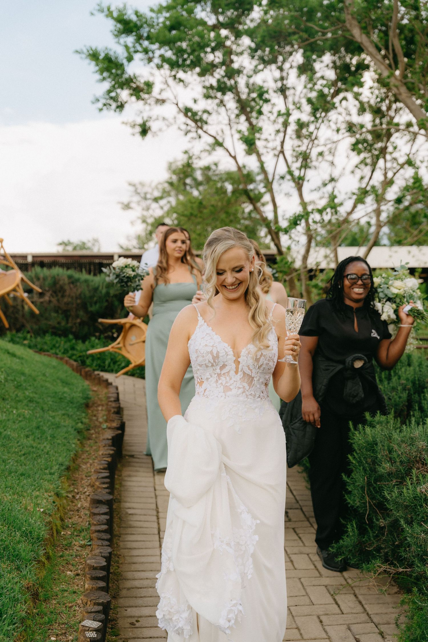 Wedding party walking and celebrating on a stone pathway surrounded by greenery.