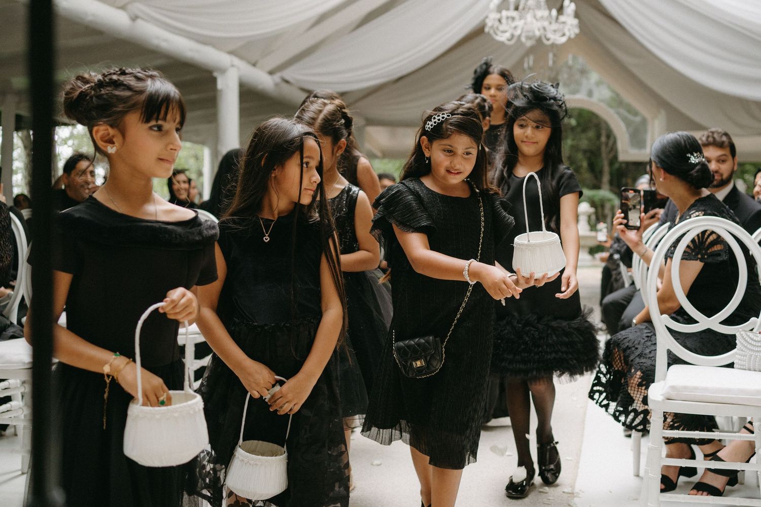 A group in all black attire gathers in an elegant white draped venue.