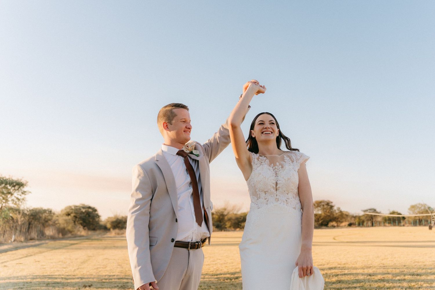 A couple dances joyfully in an open field during their wedding celebration.
