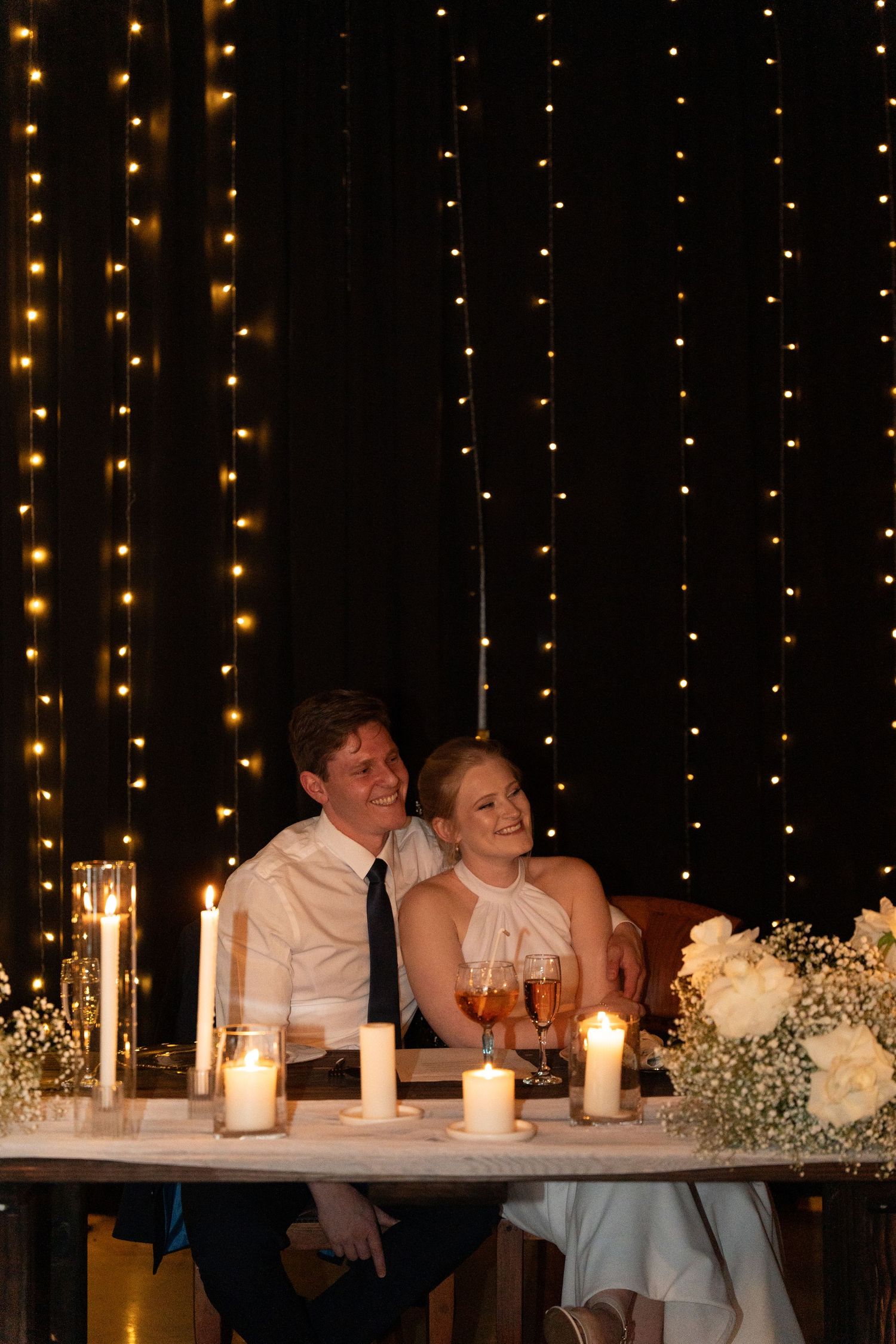 A wedding reception head table decorated with candlelight and string lights creating a romantic ambiance.