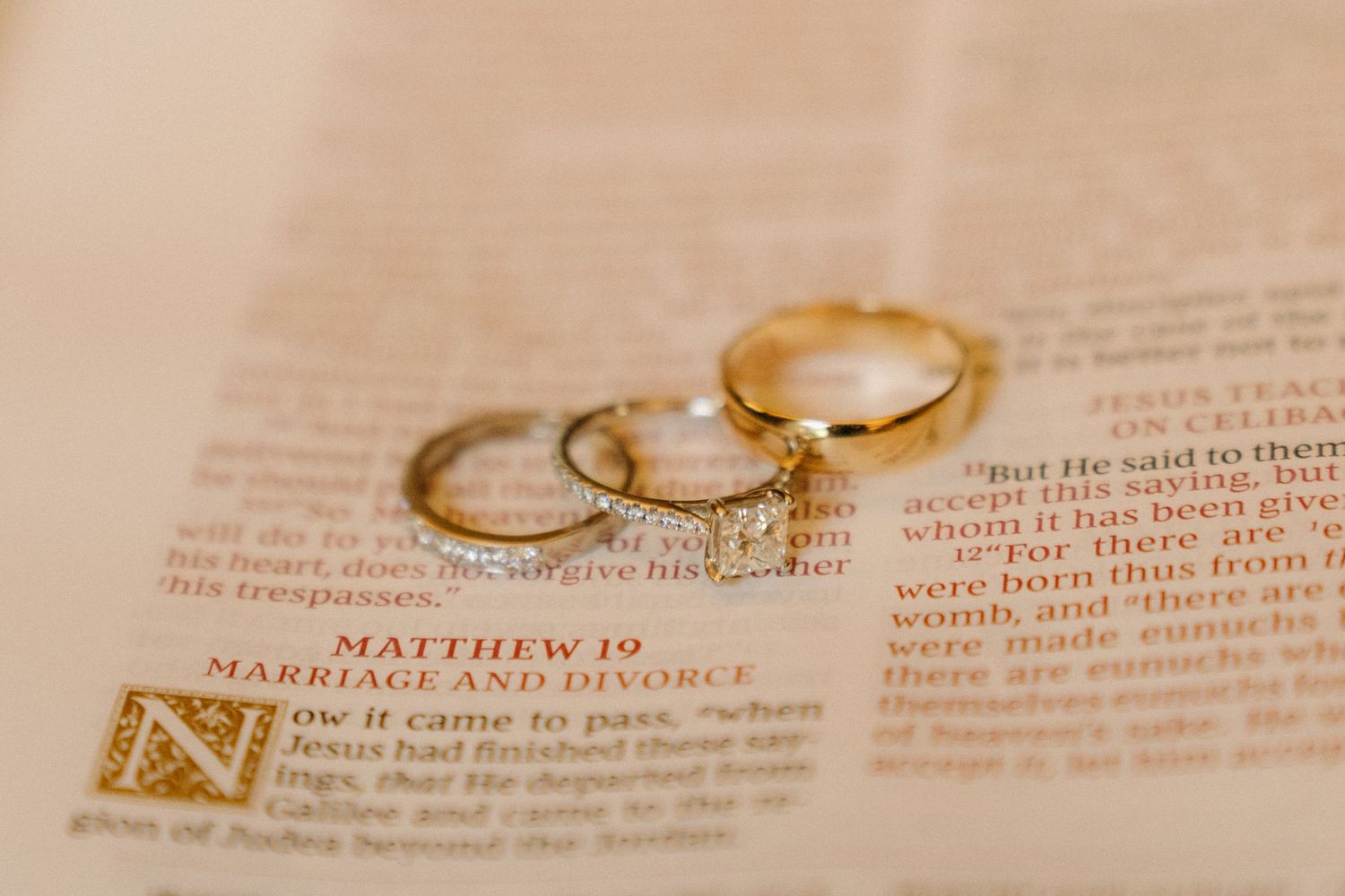 Two gold wedding rings rest on open pages of a Bible displaying text from the book of Matthew.