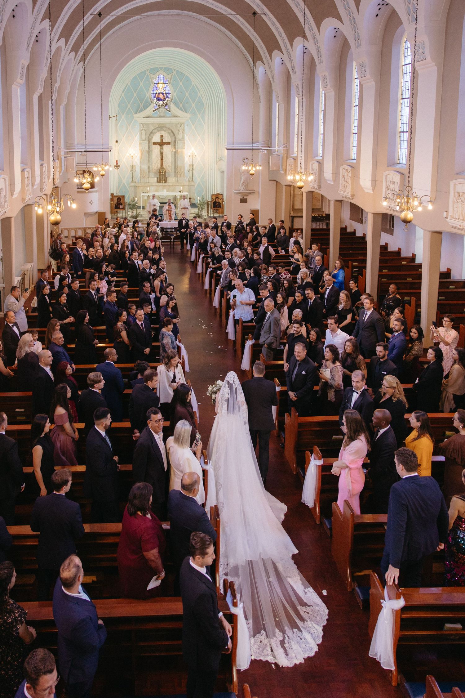 Bride walks down the aisle in a stunning cathedral-length veil at a Rosebank Catholic Church wedding ceremony.