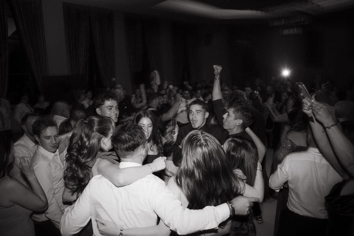 Black and white photo of a large crowd of people dancing and celebrating at a formal party or wedding reception.