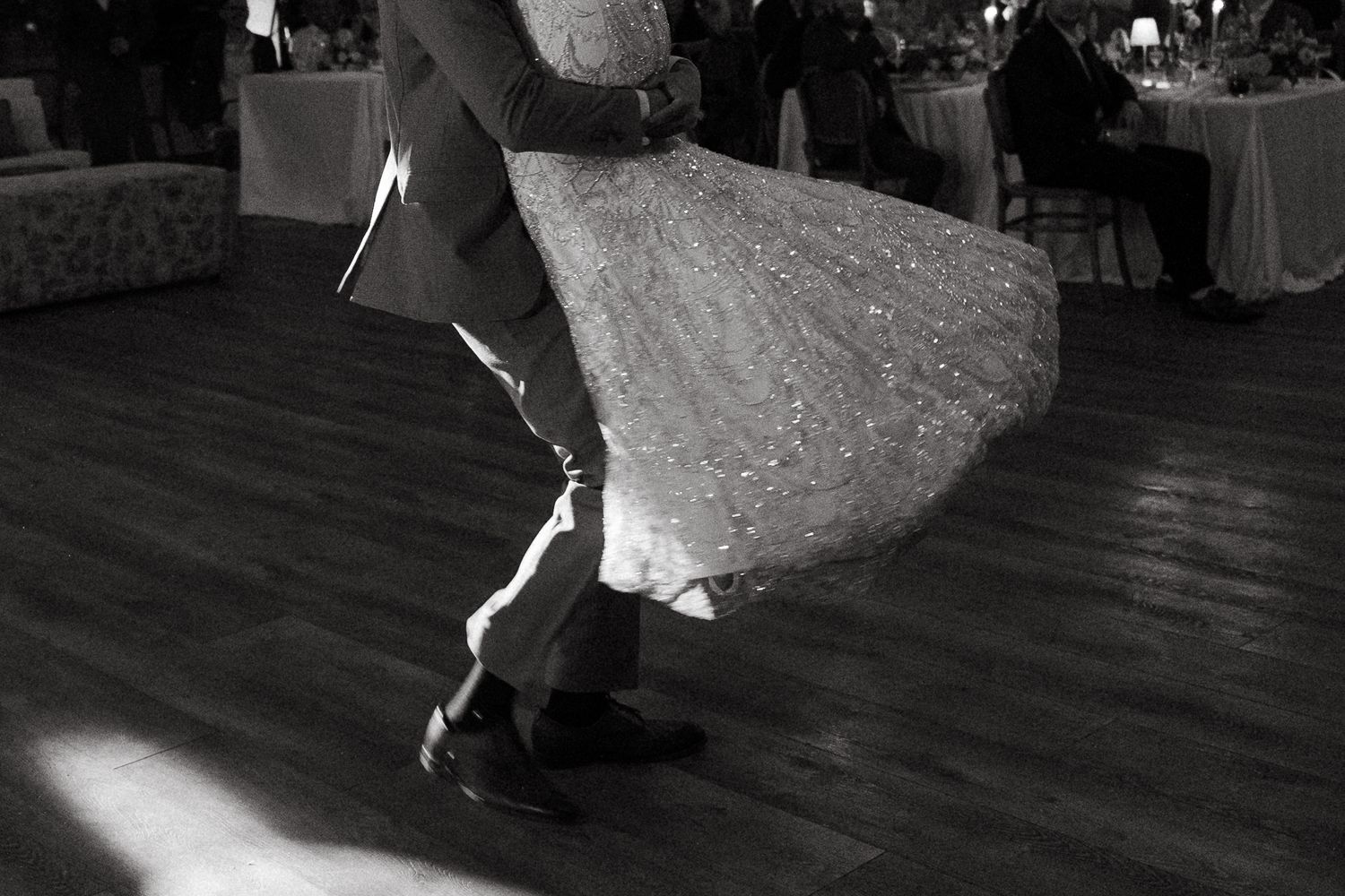 Black and white photo of a couple sharing their first dance, bride's gown swirling on a wooden dance floor.