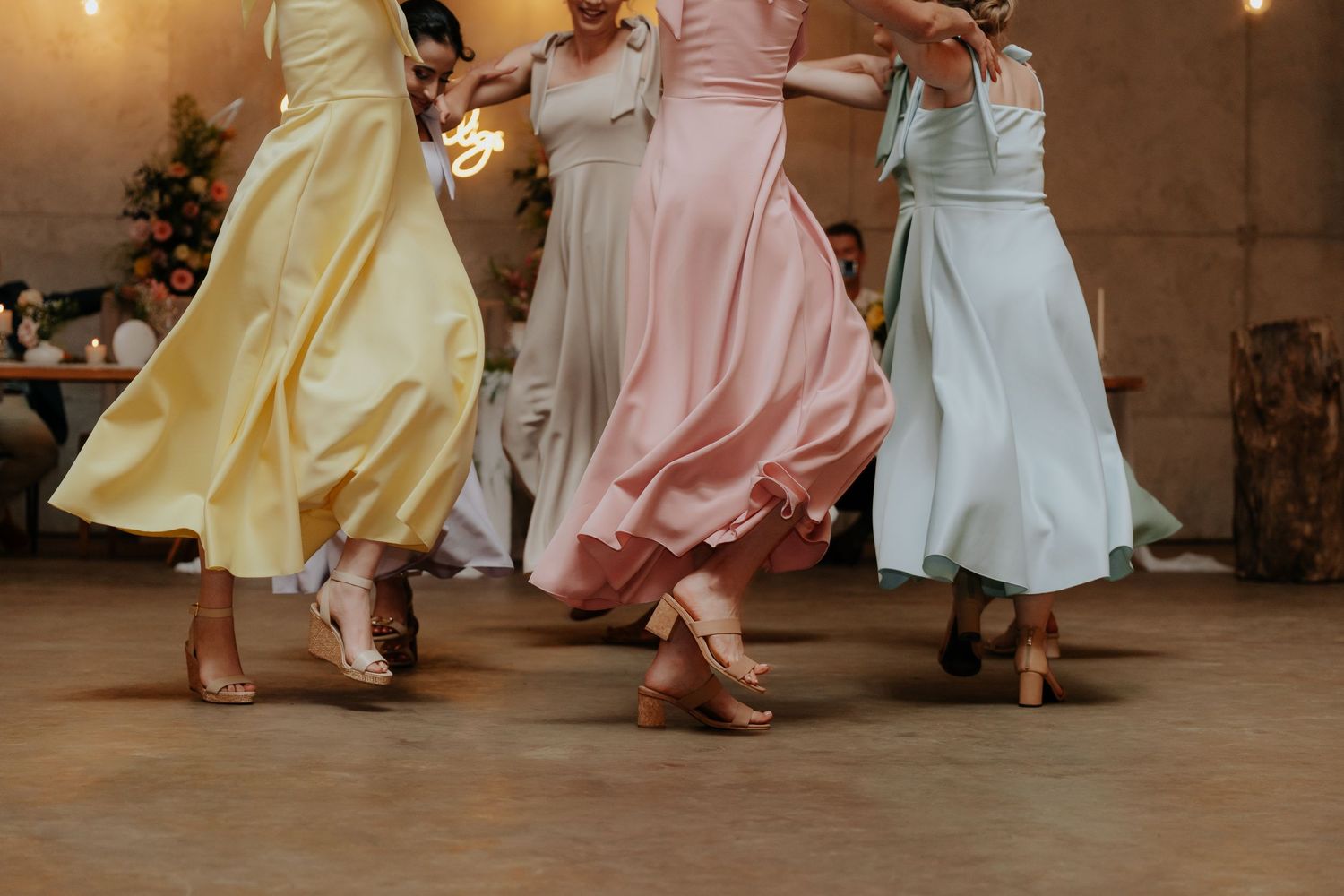 Group of dancers in pastel colored dresses twirling and dancing together on a wooden floor.