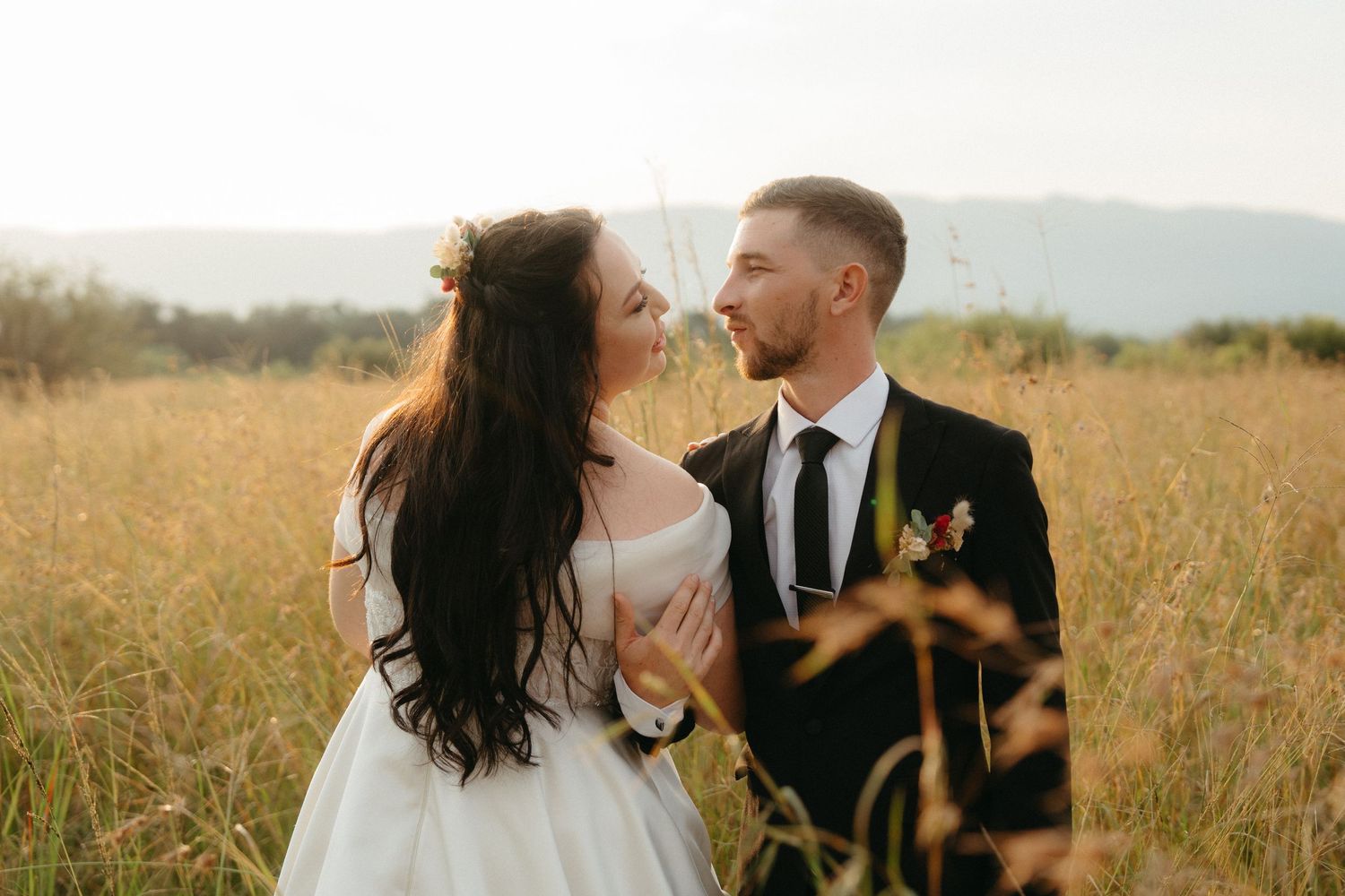 Romantic couple shares intimate moment in sunlit golden field during wedding photoshoot.