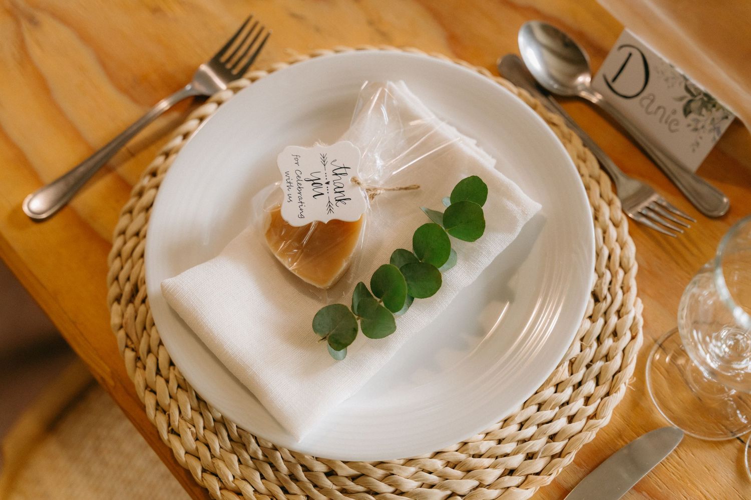 Elegant place settings with woven chargers and eucalyptus leaves on wooden table.