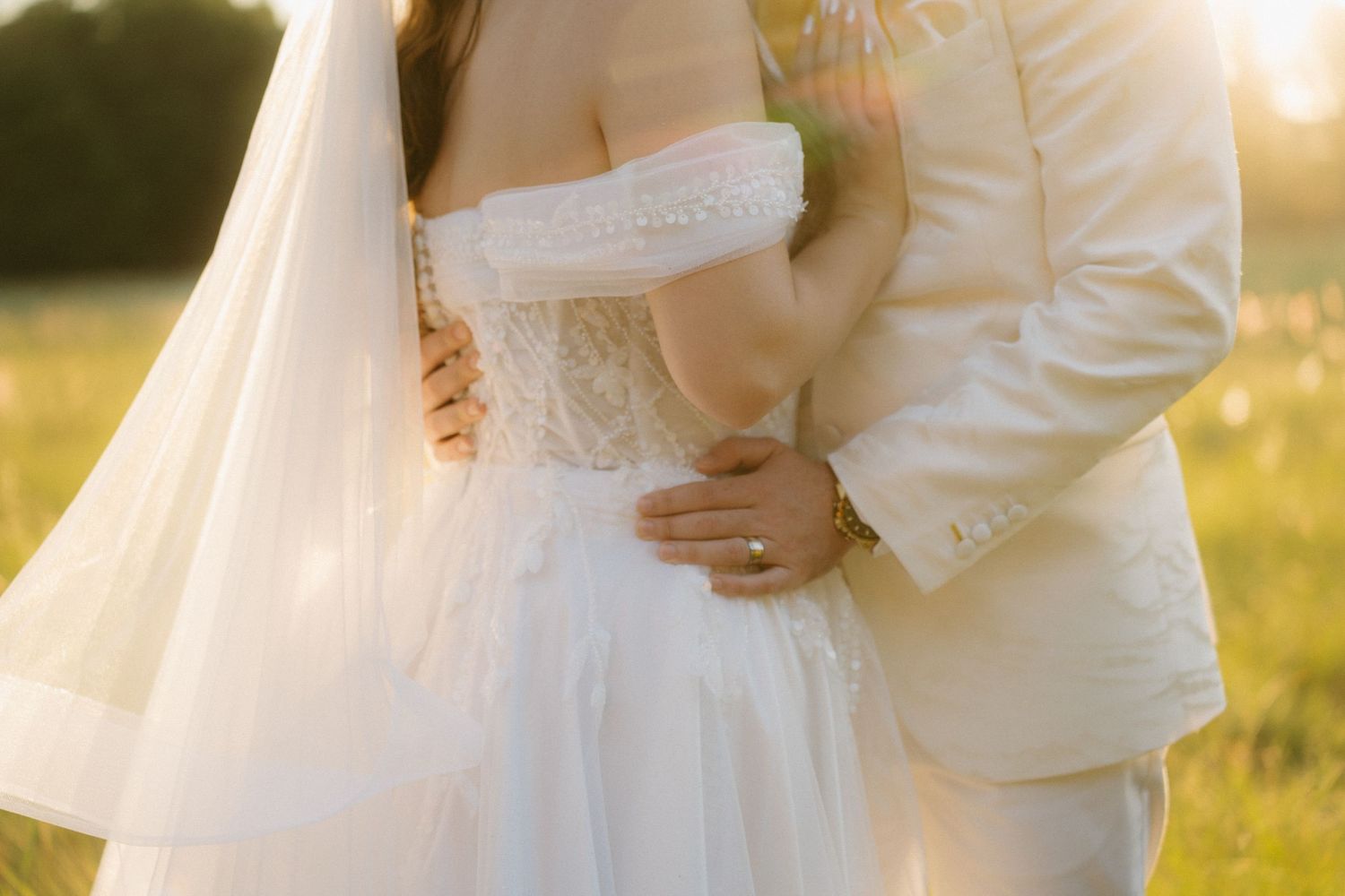 Close-up detail of white wedding dress and suit during golden hour outdoor portrait.