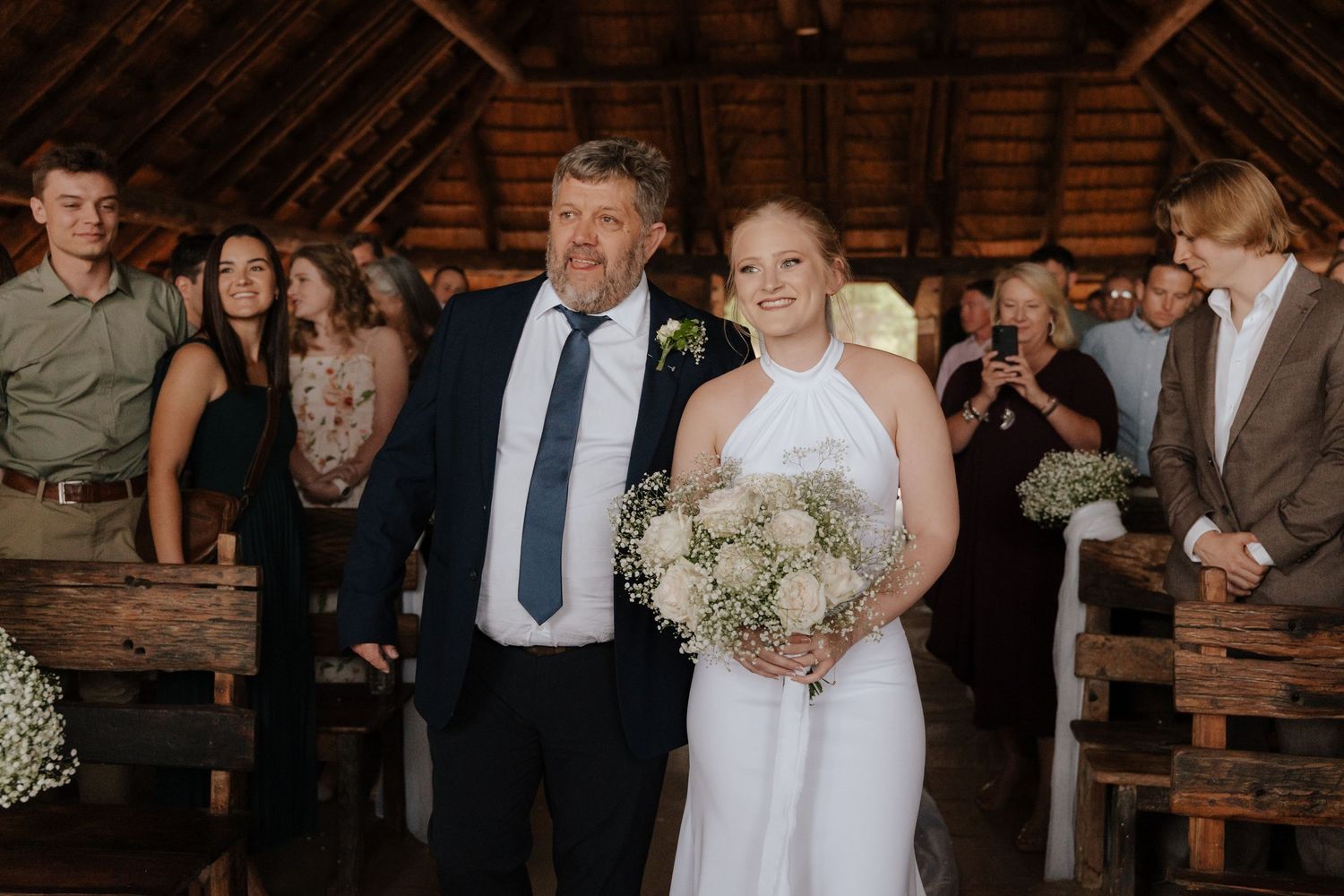 Wedding celebration in a rustic barn venue with wooden benches and natural lighting.