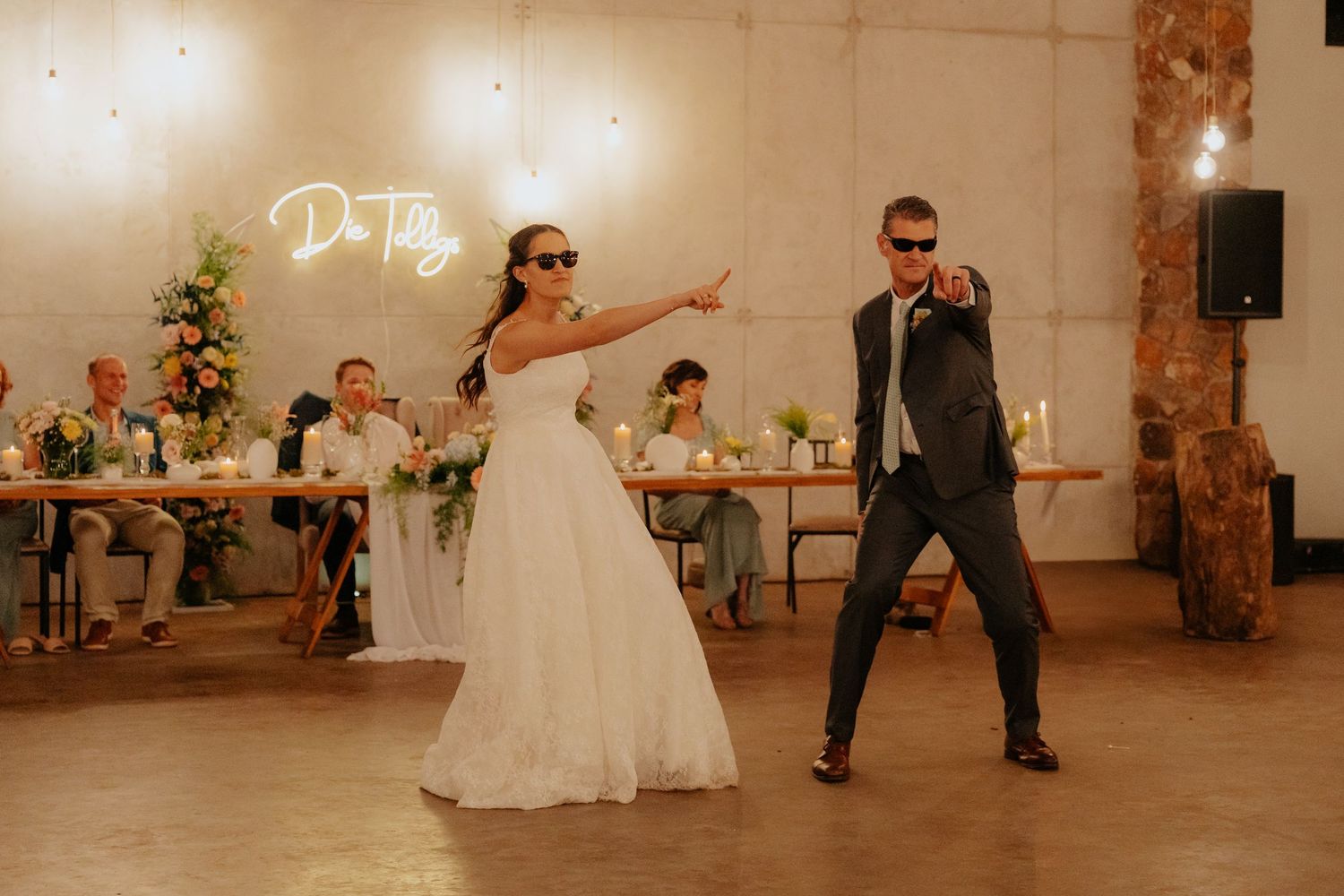 Wedding couple dances in a white-walled venue with fairy lights and floral decorations.