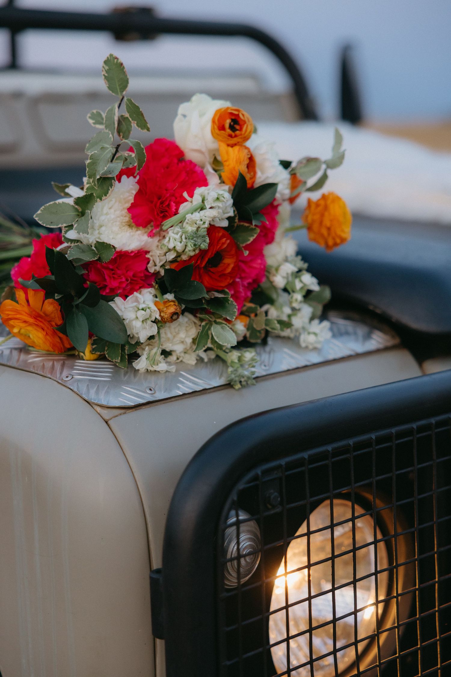 Vibrant red and orange floral bouquet arranged on the hood of a vintage vehicle.