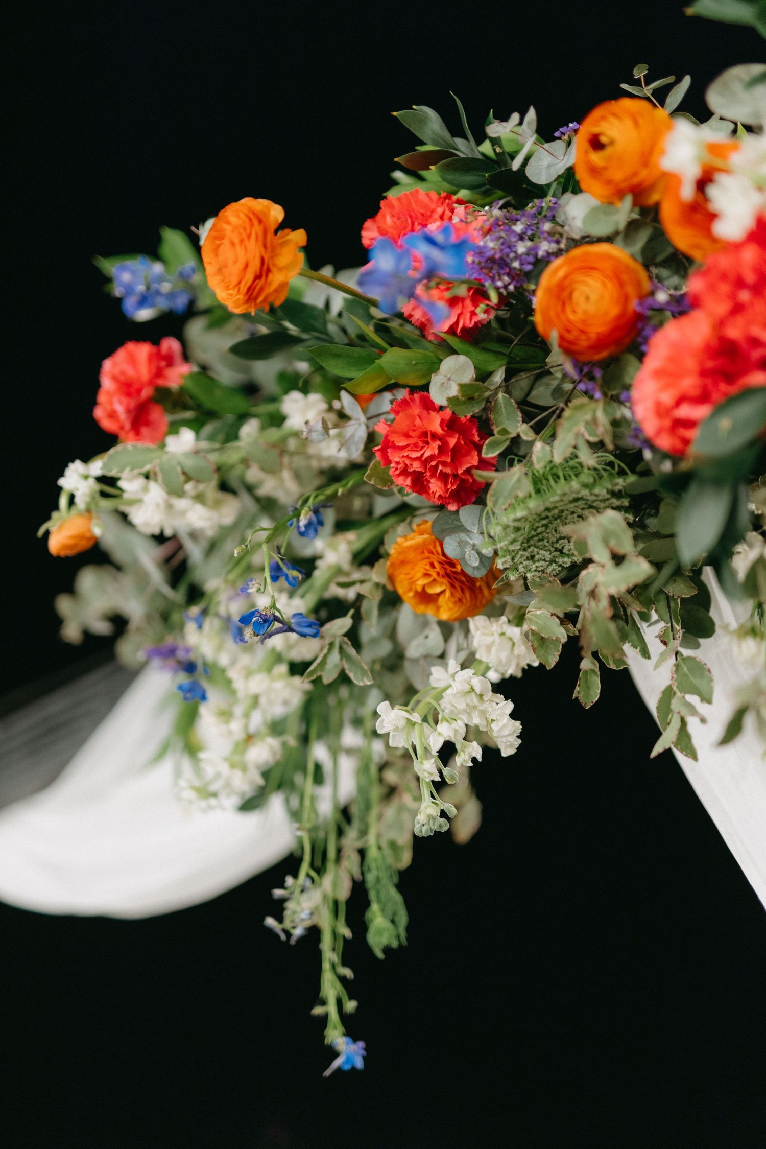 Vibrant floral arrangement with orange, blue and white flowers against dark background.