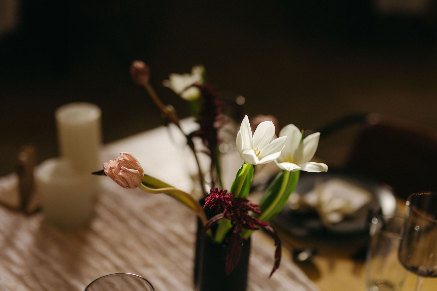 Elegant white flowers in a dark vase on a wooden table with candles creating a moody ambiance.