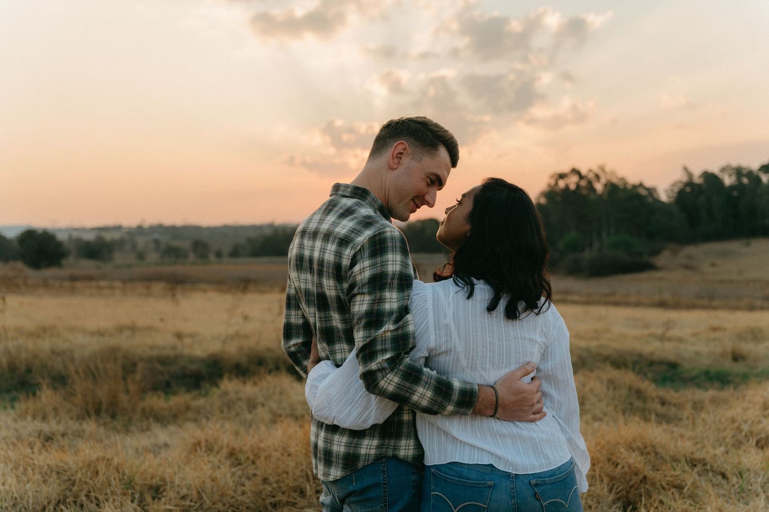 Couple sharing an intimate moment in a field during golden hour.