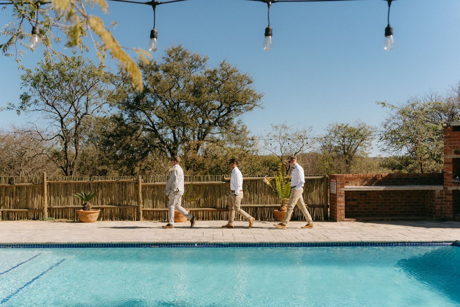 Three groomsmen walk alongside a sparkling outdoor pool at Grin Court in Limpopo