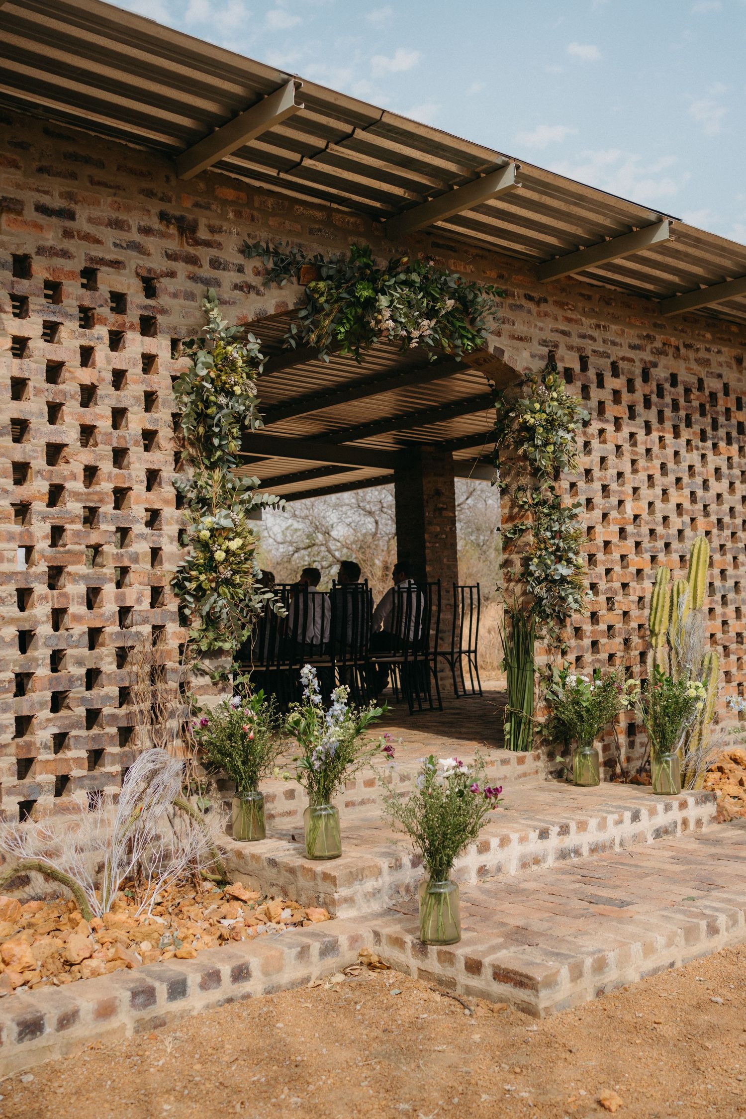 Architectural detail of a modern brick wall with geometric patterns and wooden pergola creating an outdoor living space.