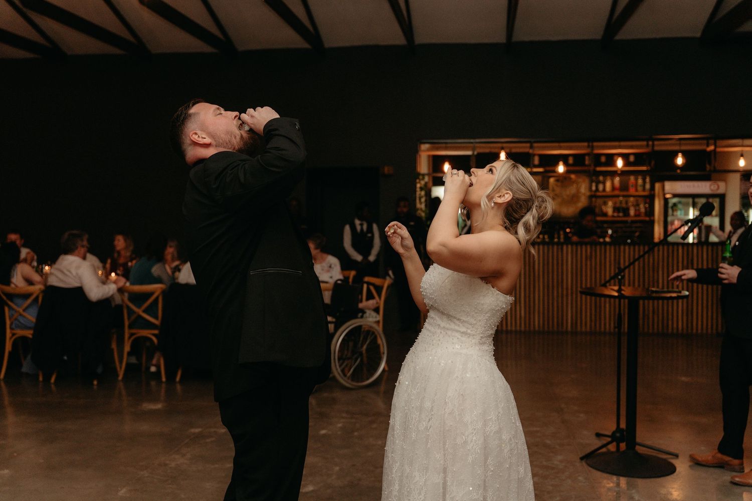 A couple shares a romantic dance on a dimly lit wooden dance floor at their wedding reception.