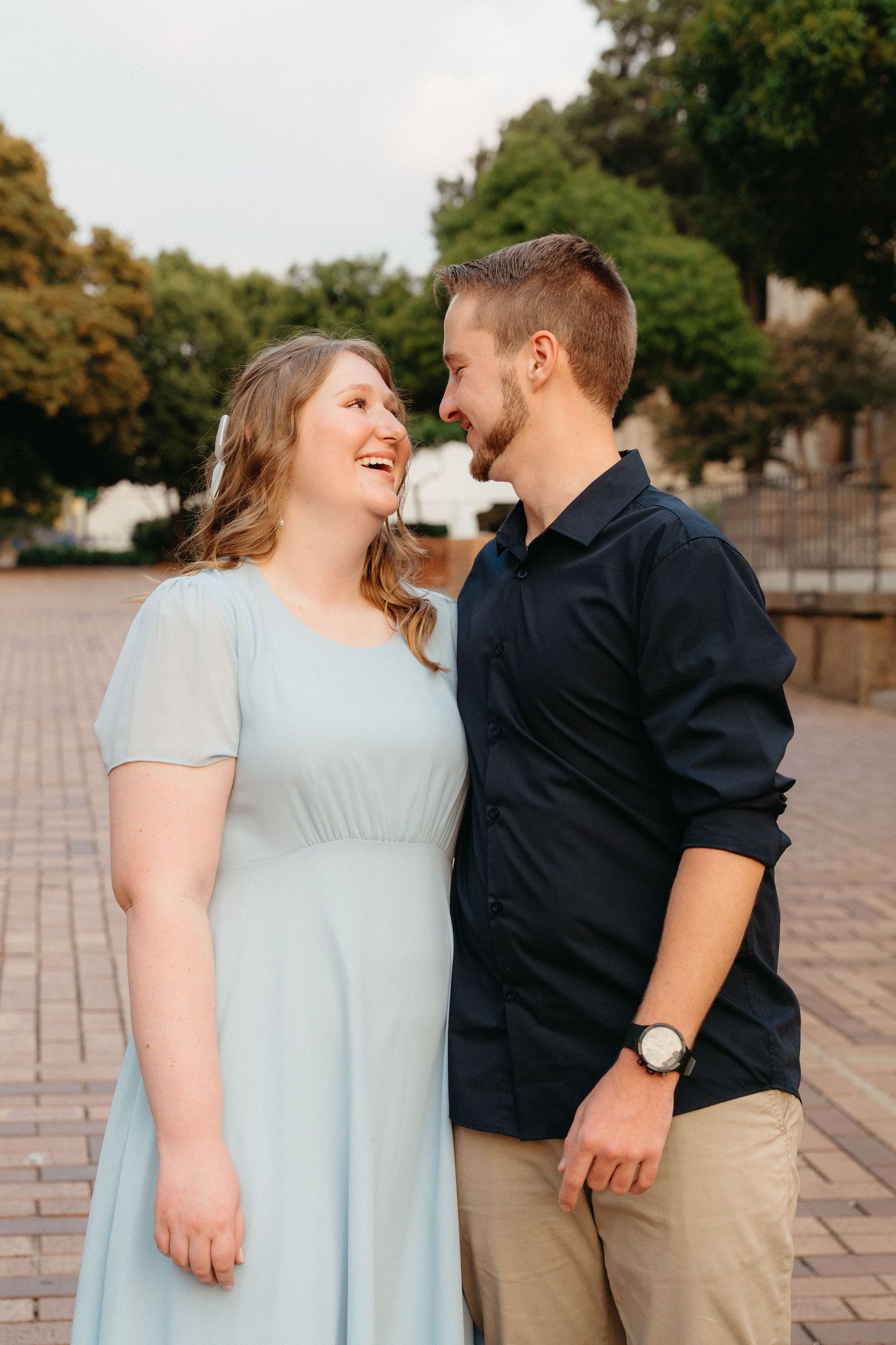 A couple shares joyful laughter together during an outdoor photoshoot on brick pavement.