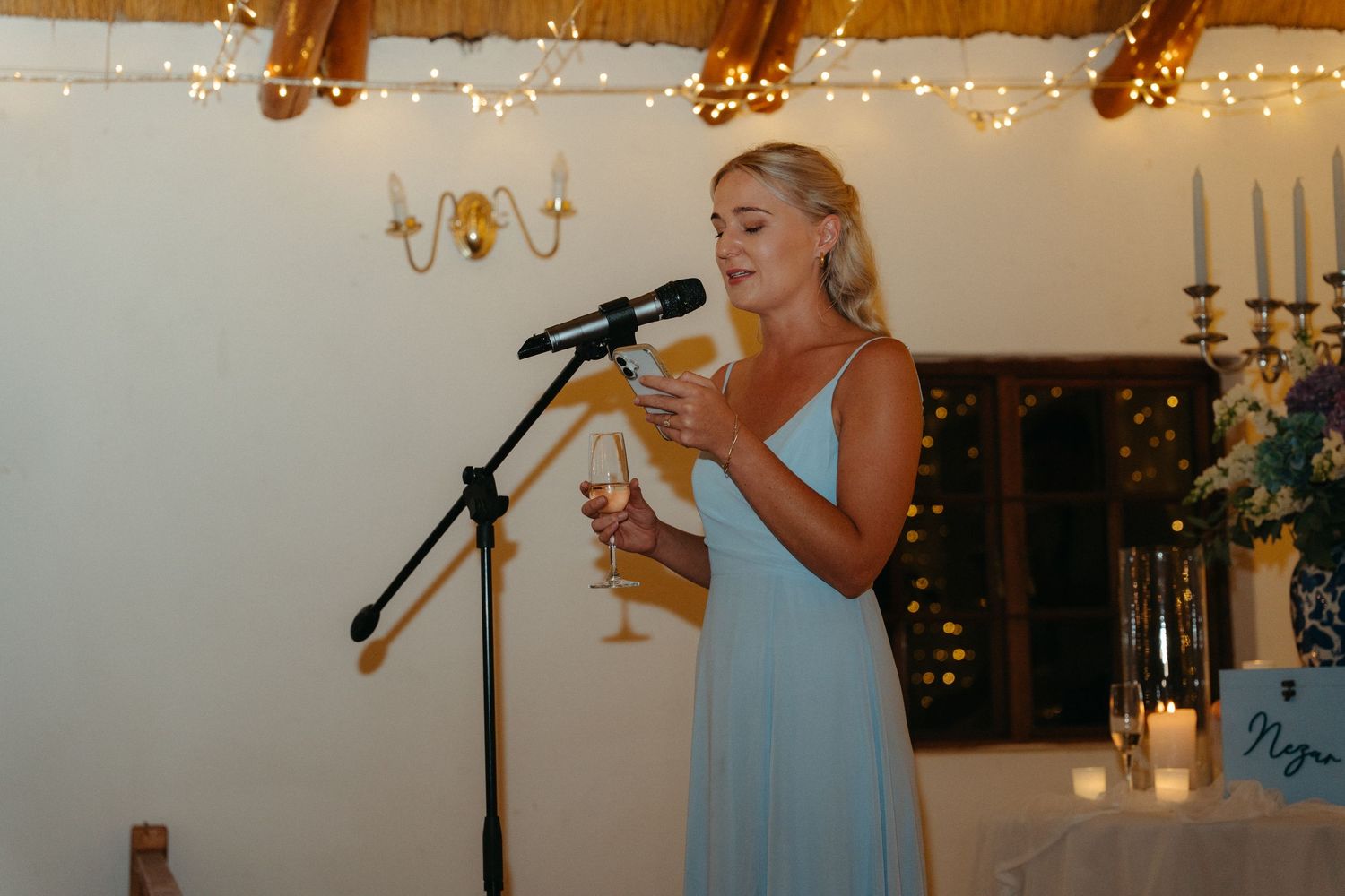 A wedding reception venue decorated with string lights and candles features guests enjoying champagne toasts.