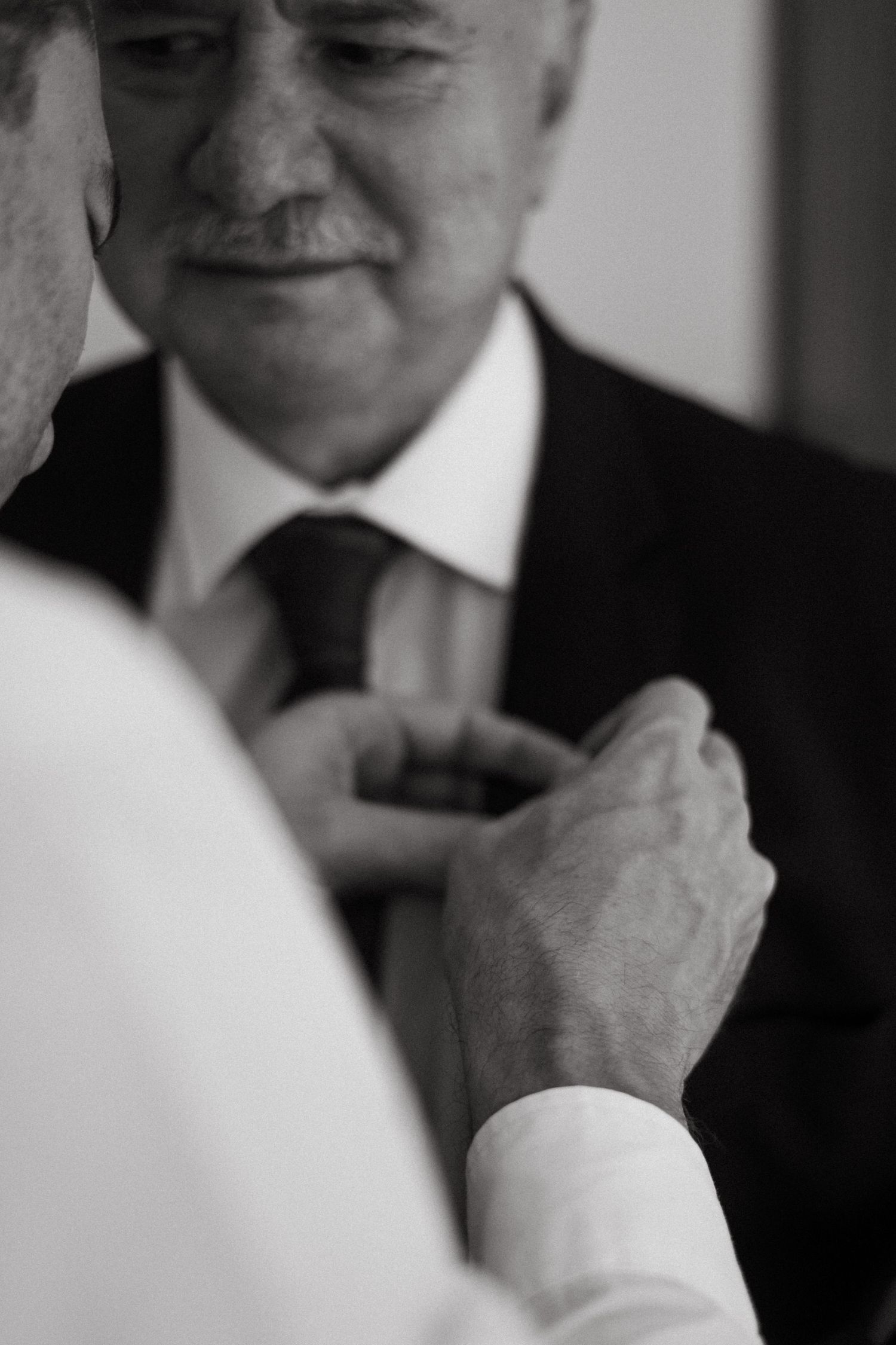 Close-up black and white photo of formal attire being adjusted during wedding preparations.