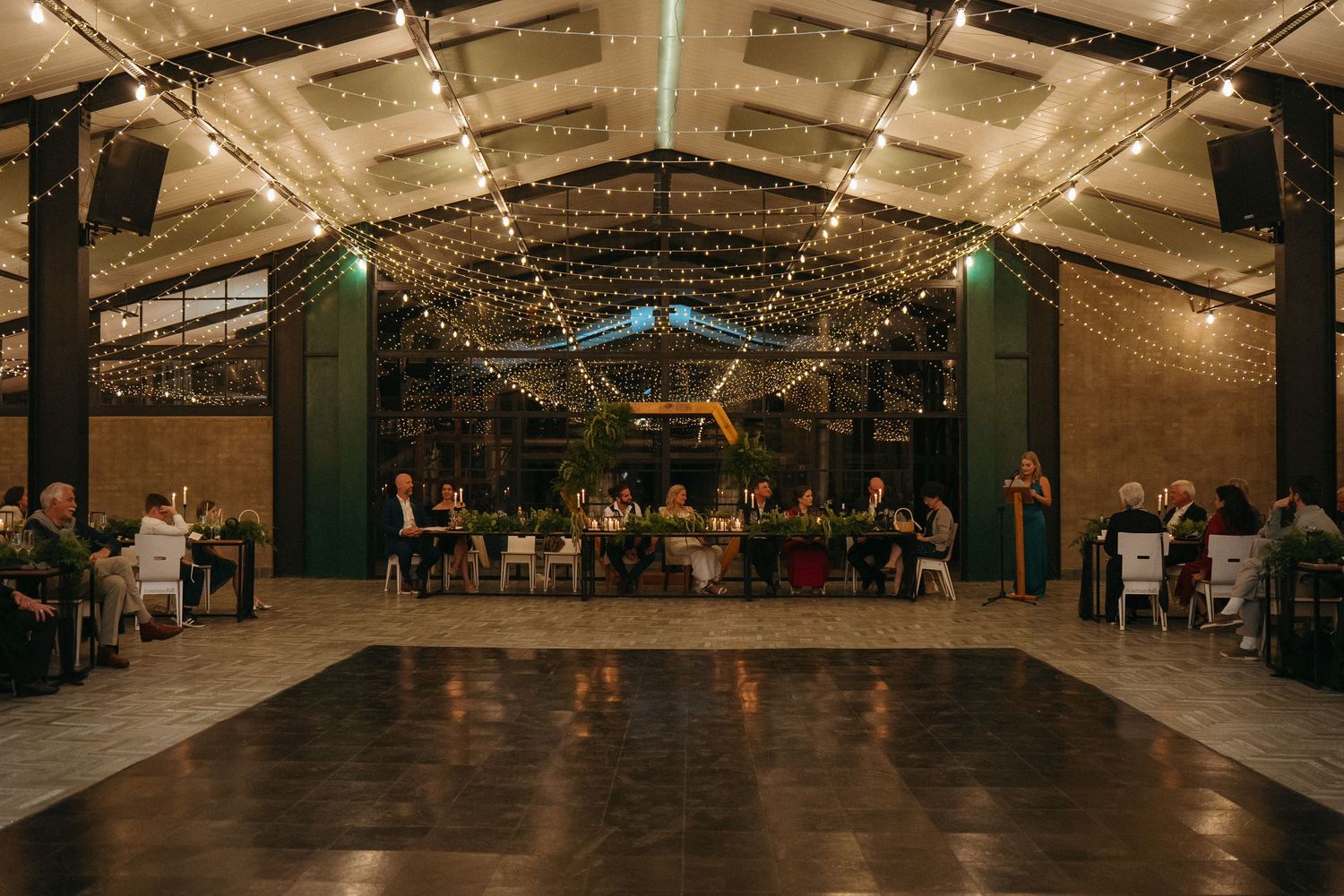Elegant wedding reception in a barn venue with string lights overhead and guests seated at decorated tables.