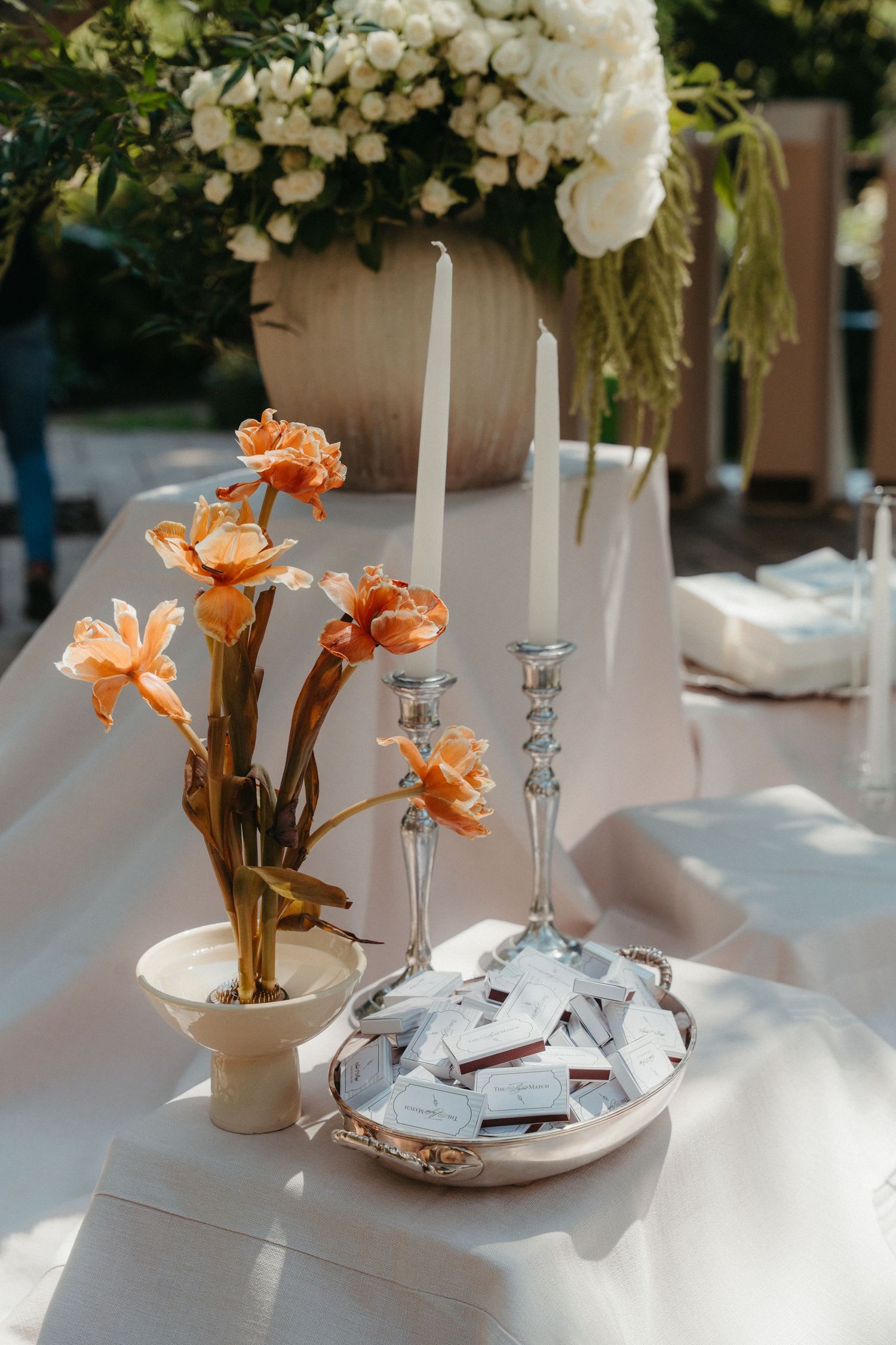 Elegant wedding table with orange flowers, silver candlesticks, white candles, escort cards on a tray, and white floral centerpiece.