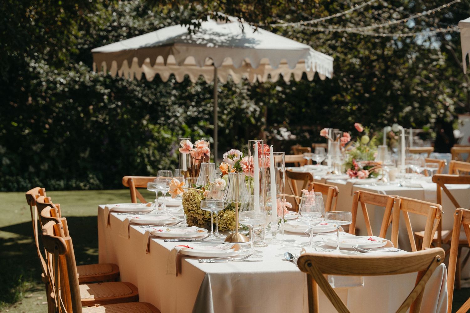 Beechwood Gardens Elegant outdoor wedding reception table set with floral centerpieces under a scalloped umbrella on a sunny day.