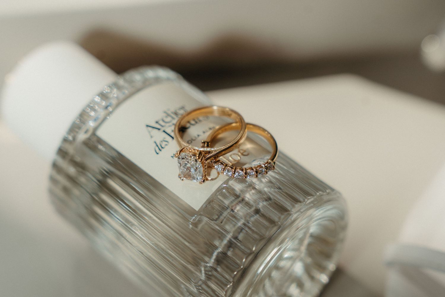 Two gold wedding rings and a diamond engagement ring resting on a crystal glass perfume bottle.