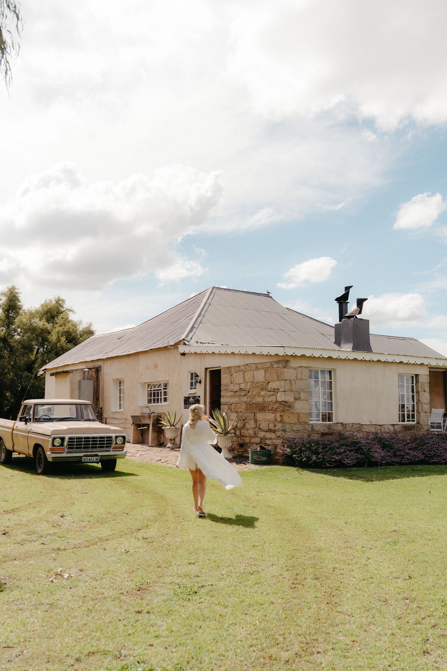 Bride in white dress twirling on lawn before rustic stone farmhouse in the Free State