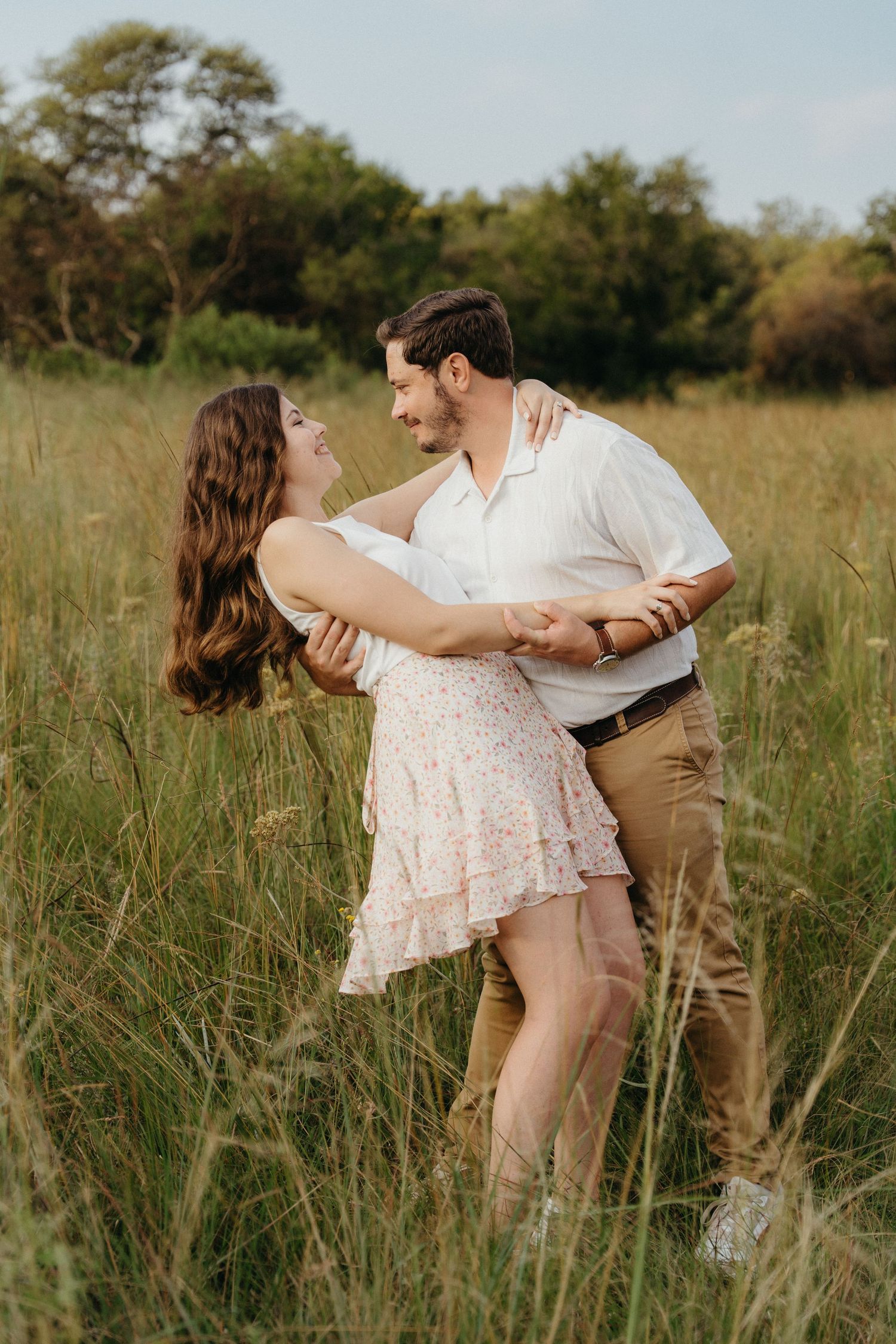 A couple dances romantically in a lush green meadow, the woman in a floral dress gazing up at her partner.