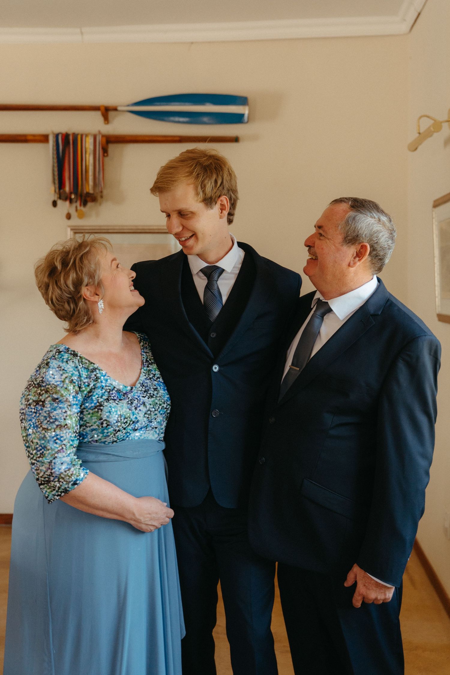Three people in formal attire share a candid moment and laughter while standing together in a room.