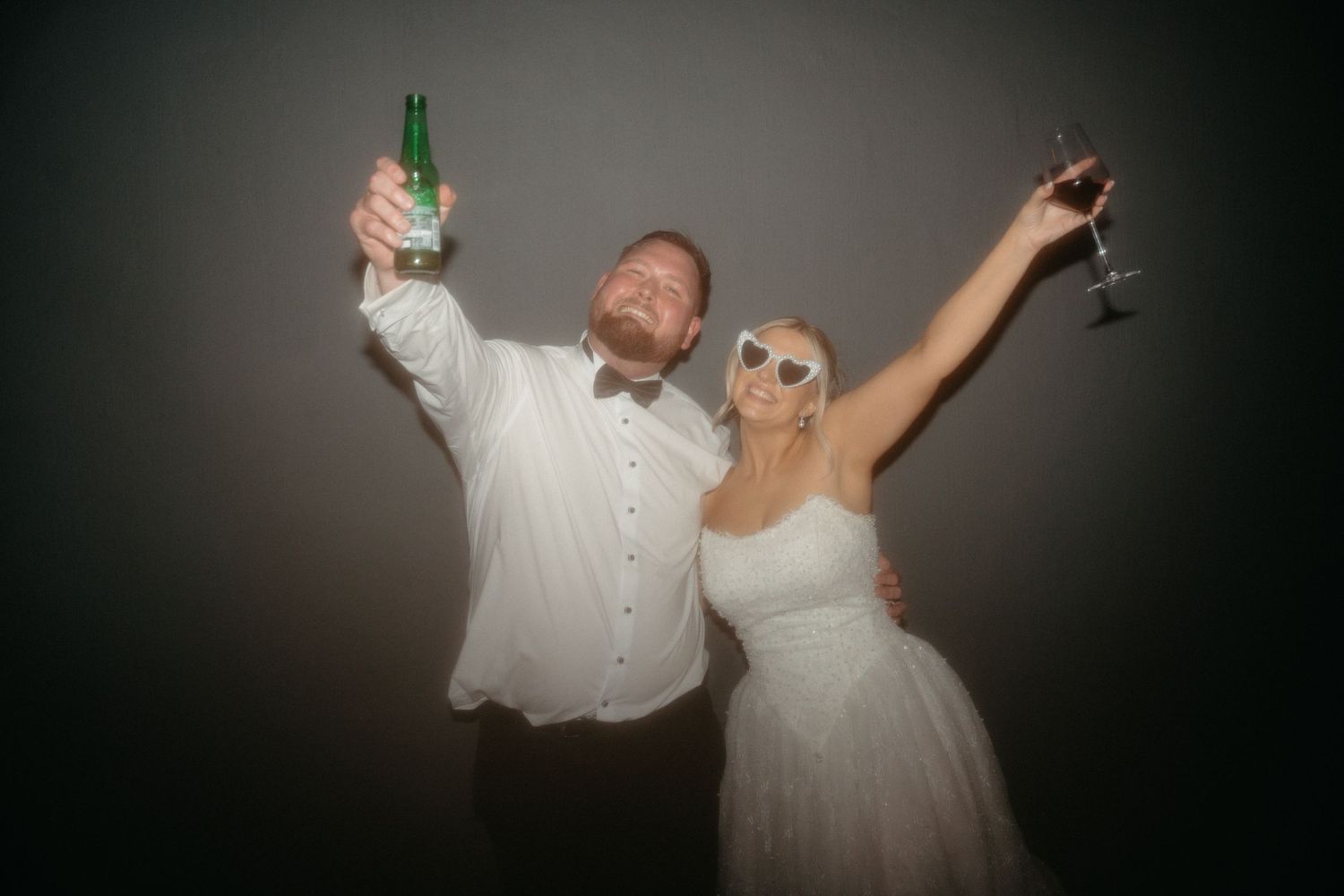 Wedding couple dances and celebrates joyfully on the dance floor in a dark reception venue with dramatic lighting.
