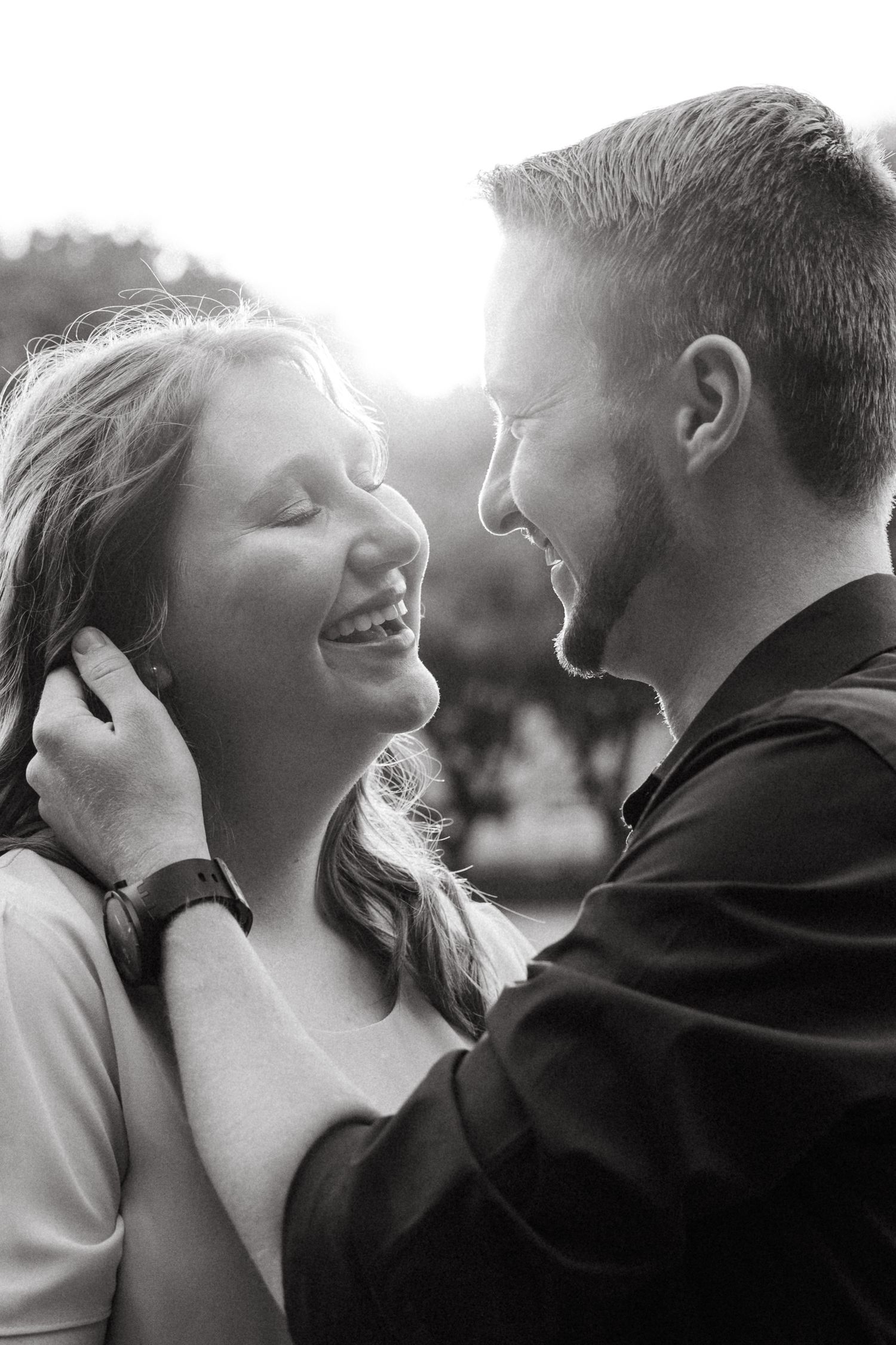 A romantic black and white portrait of a couple sharing an intimate laughing moment together in natural sunlight.