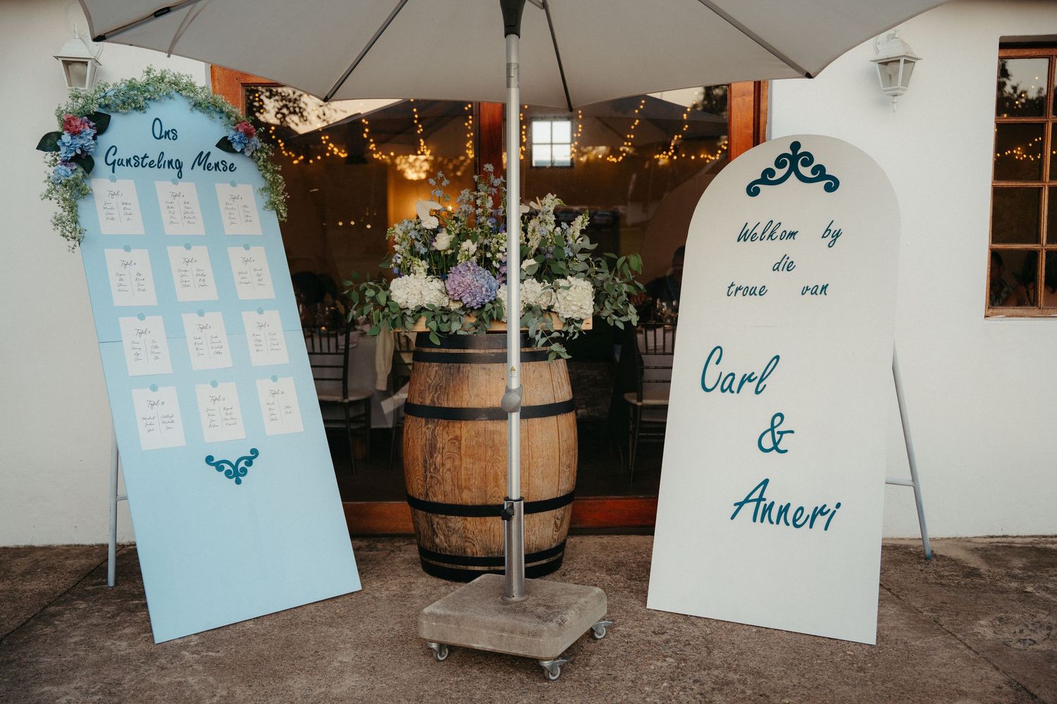 Light blue wedding seating cards with elegant calligraphy hang from strings at an indoor reception venue.