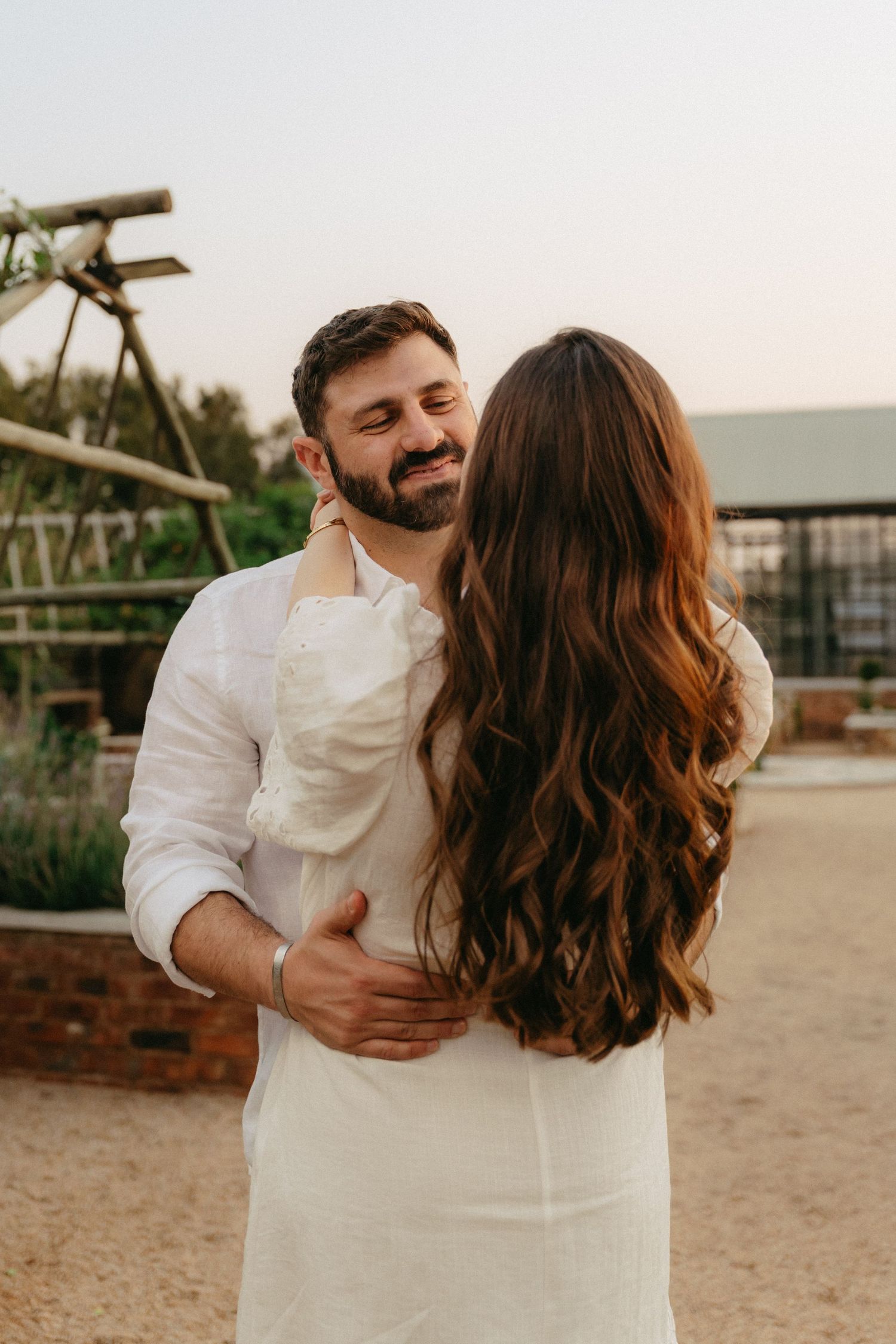Couple in coordinated white outfits sharing tender moments at sunset in an outdoor setting.
