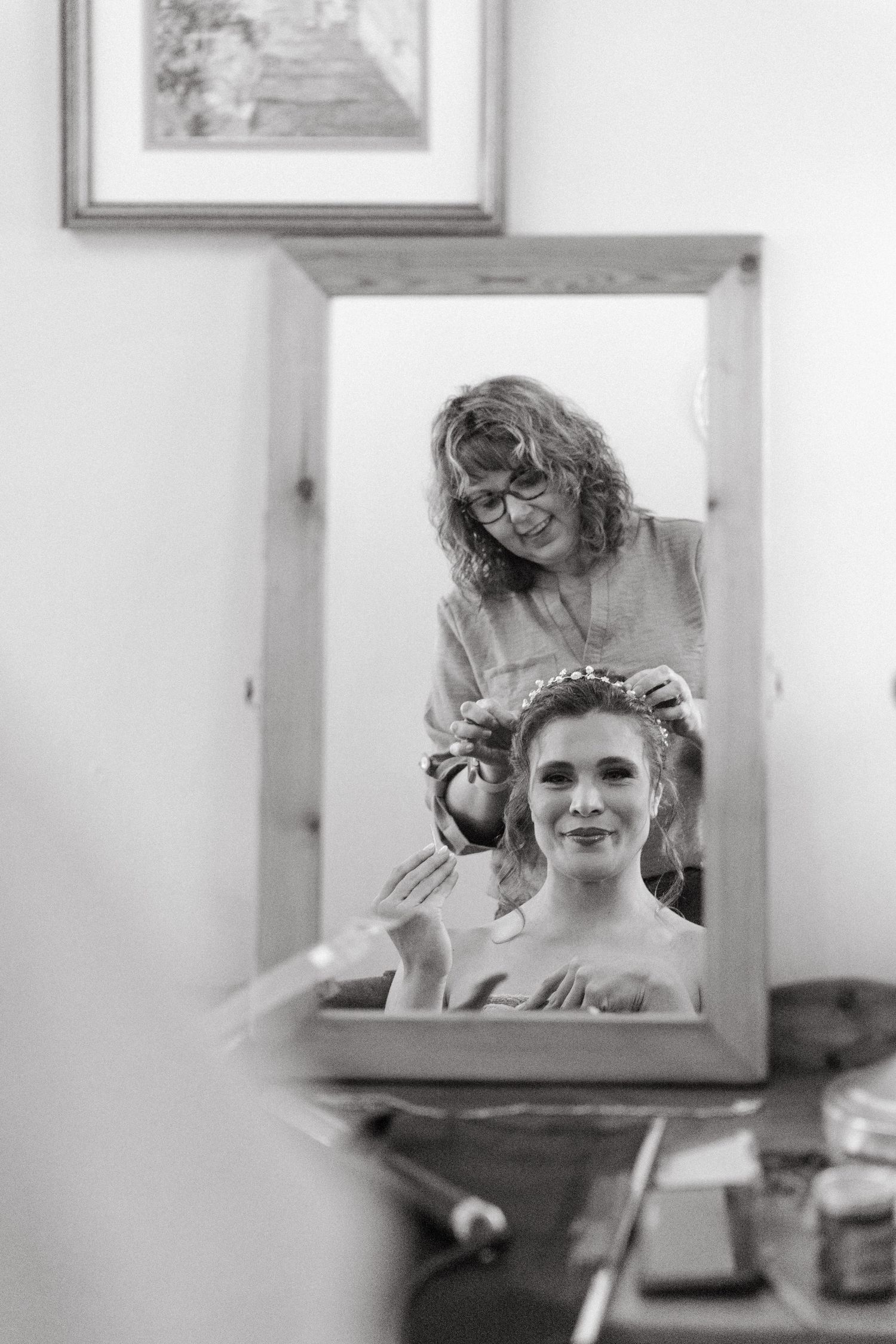 Black and white reflection in mirror shows wedding day hair preparation.